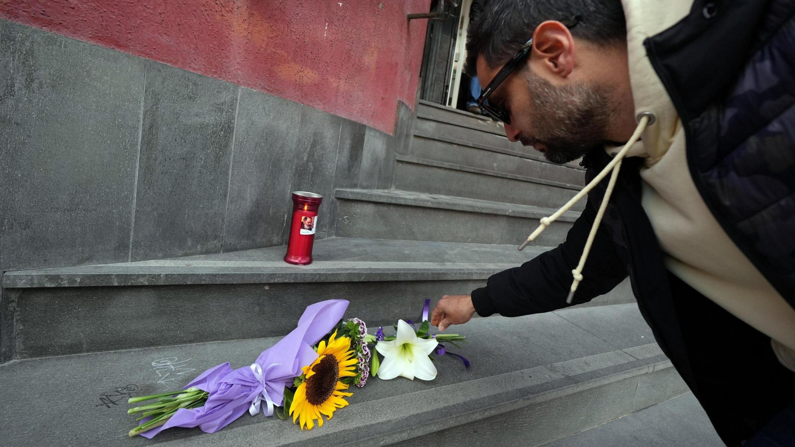 A man placing flowers on a step, above which a red candle is lit