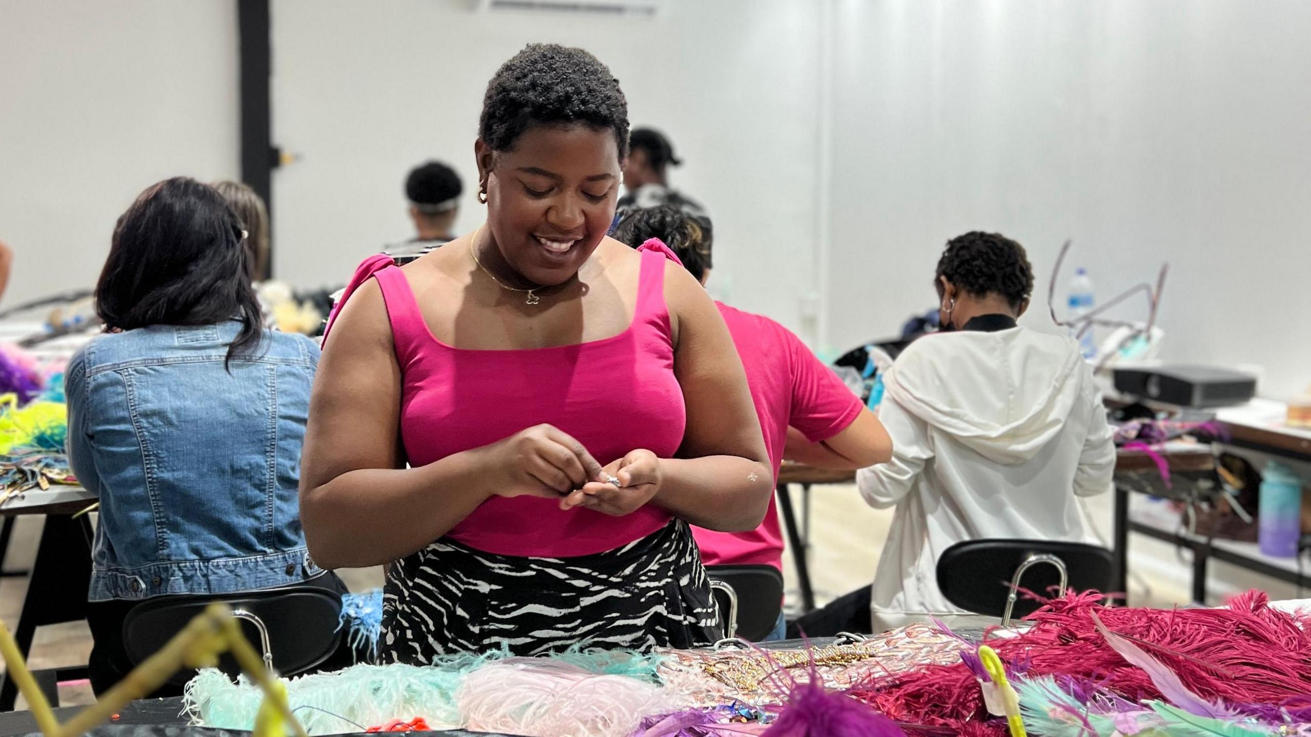 Danii McLetchie stands at a table full of feathers and sequins. She looks down at her hand while sorting through the materials. 