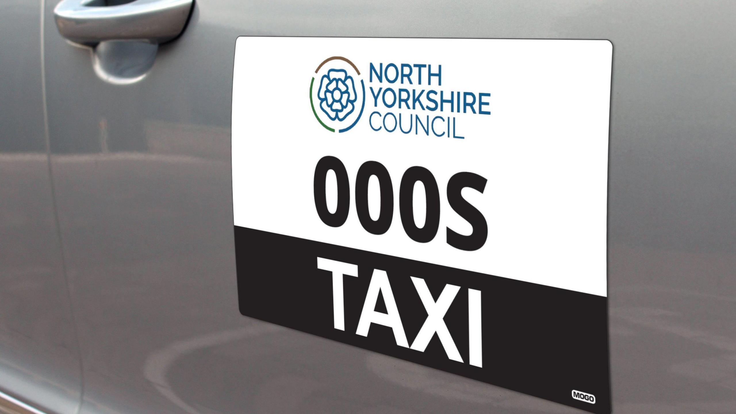 The side of a silver taxi with a sign reading "North Yorkshire Council taxi"