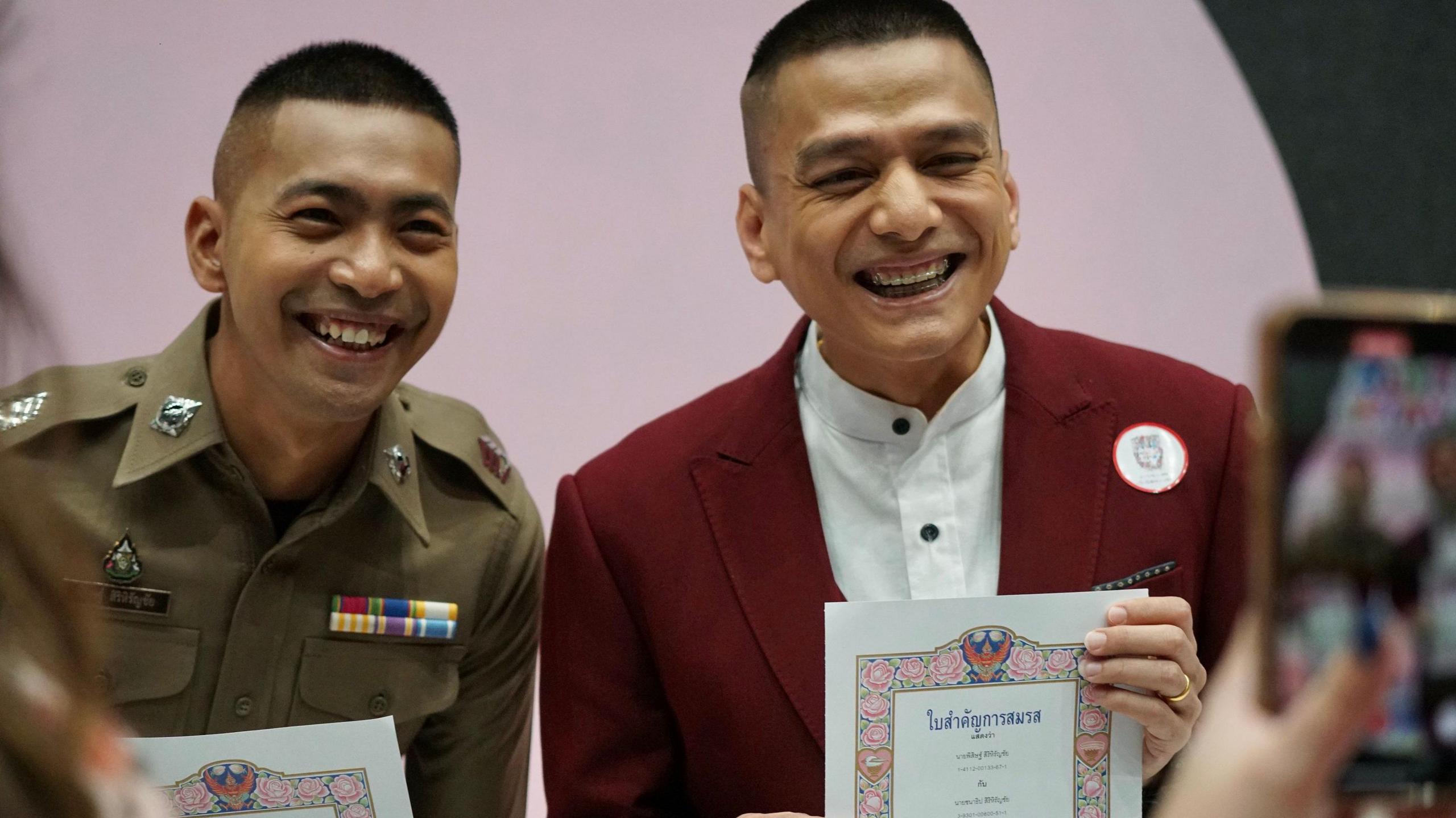 Pisit "Kew" Sirihirunchai (L) in police uniform and his partner Chanatip "Jane" Sirihirunchai in a red suit smile while holding their marriage certificates