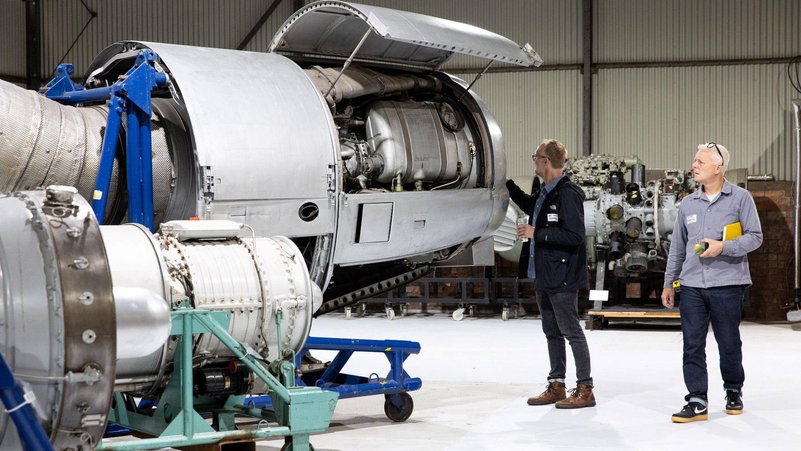 Two men walk alongside large aircraft engines which are on display at the Bristol Aerospace Collection.