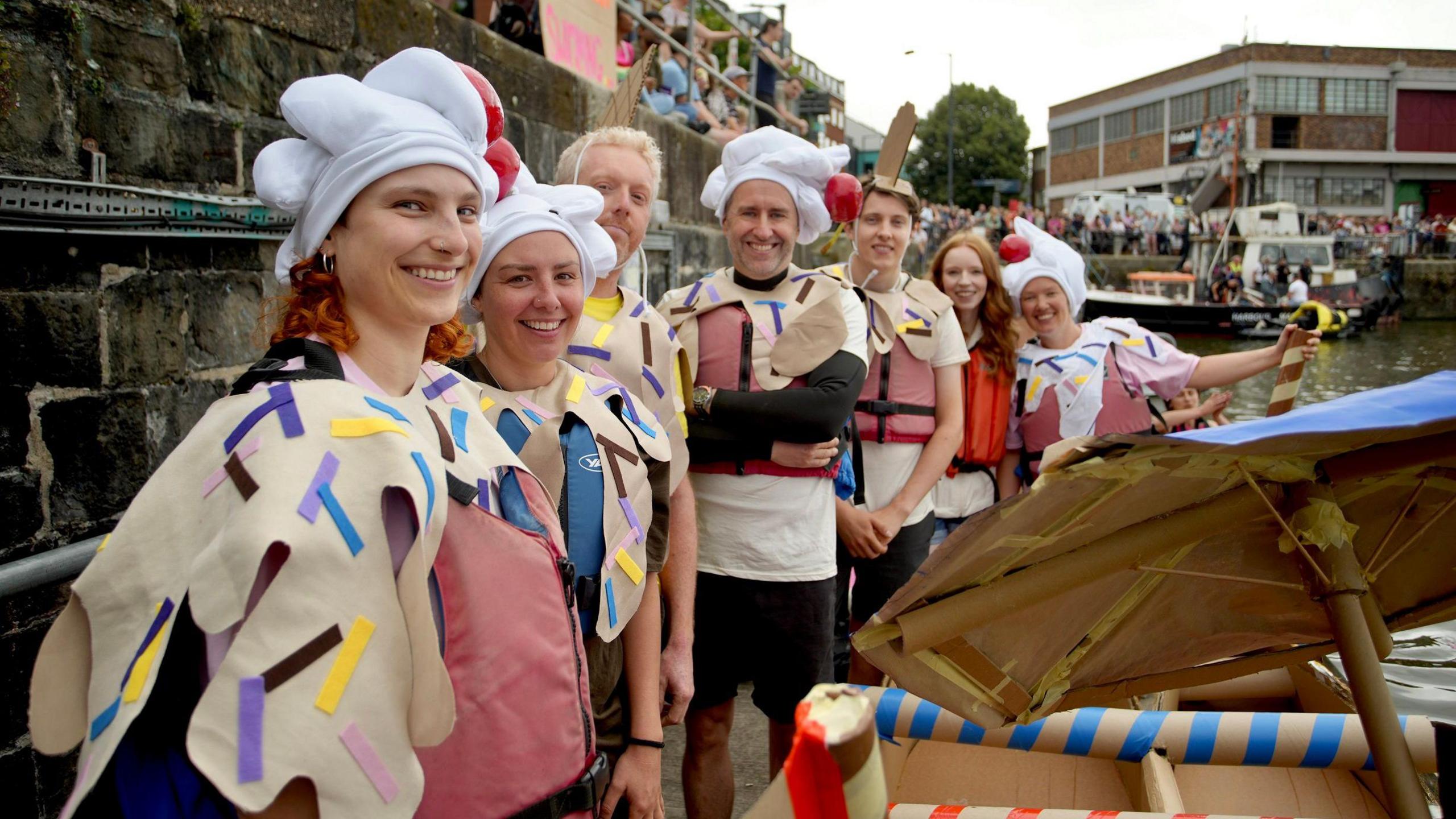 A group of people about to take part in the cardboard boat race at the Bristol Harbour Festival smile for the camera