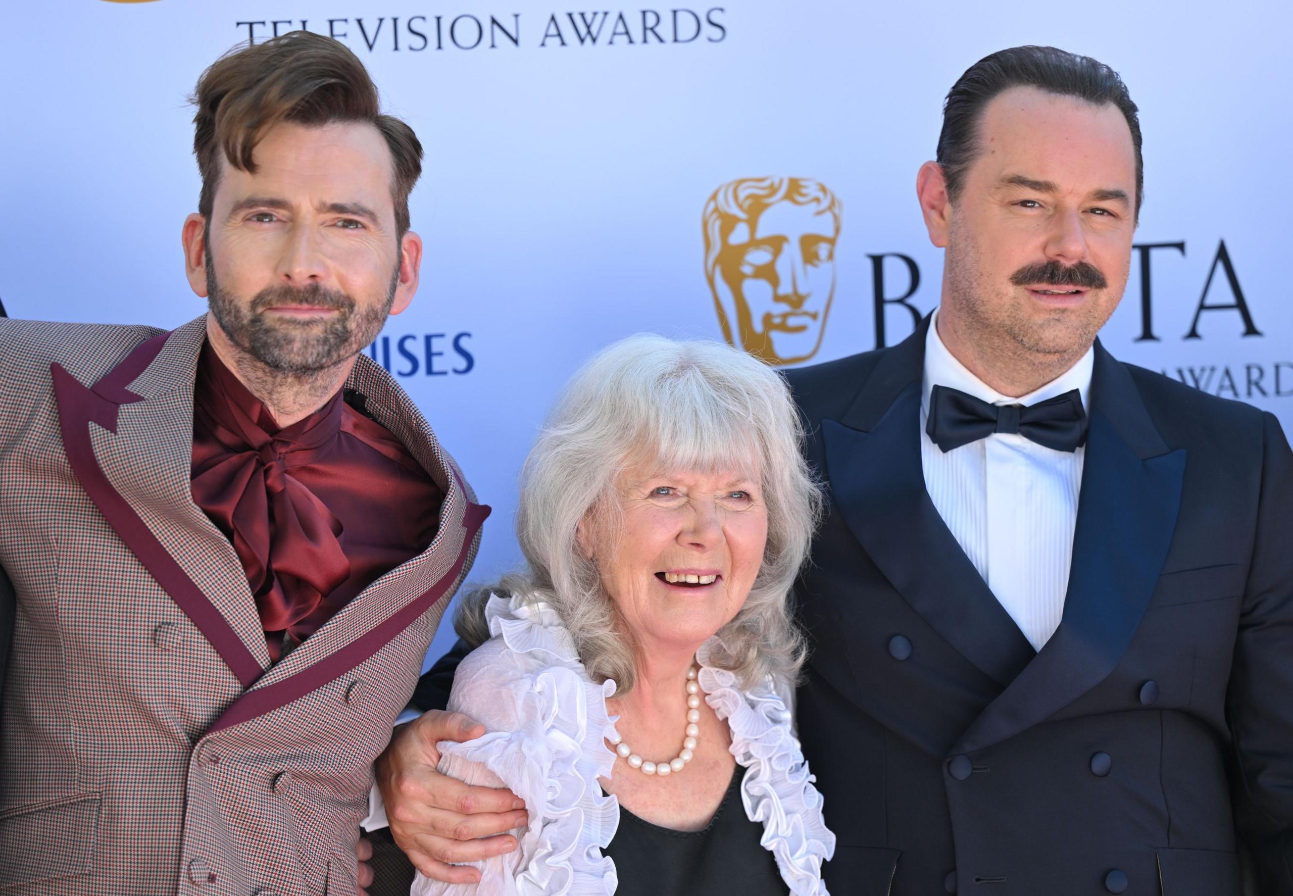 Jilly Cooper standing between David Tennant and Danny Dyer, who has his arm around her, on the red carpet at the 2025 Bafta TV Awards