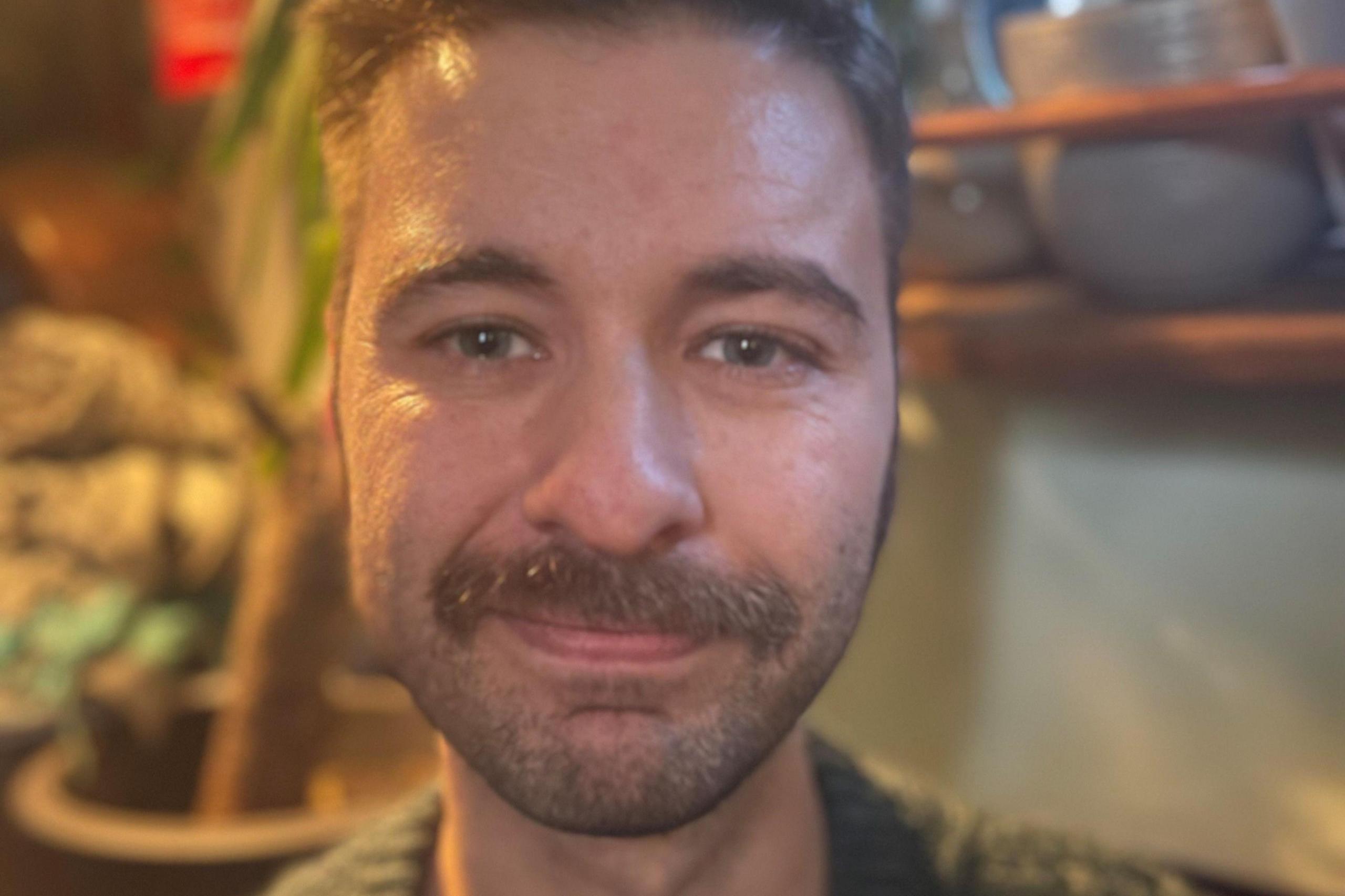 A man with a moustache looks into the camera from inside a houseboat