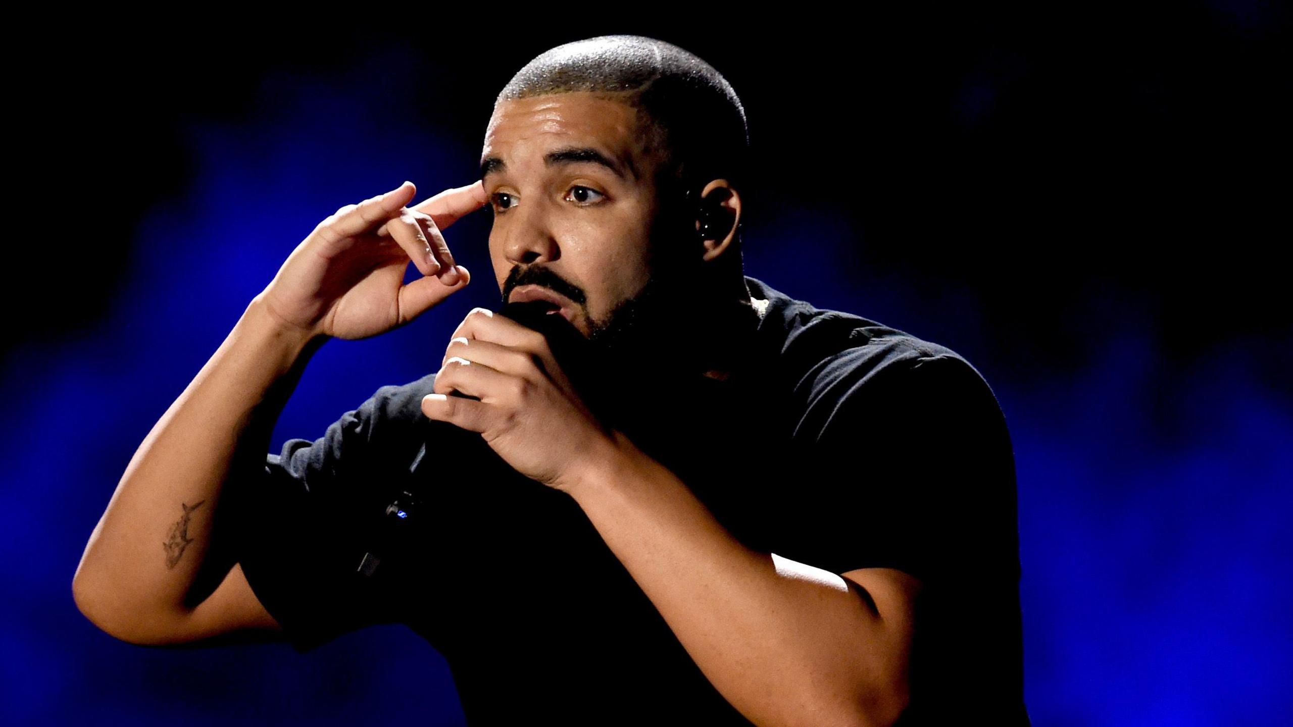 The Canadian musician Drake, dressed in black, performs against a marbled blue background.