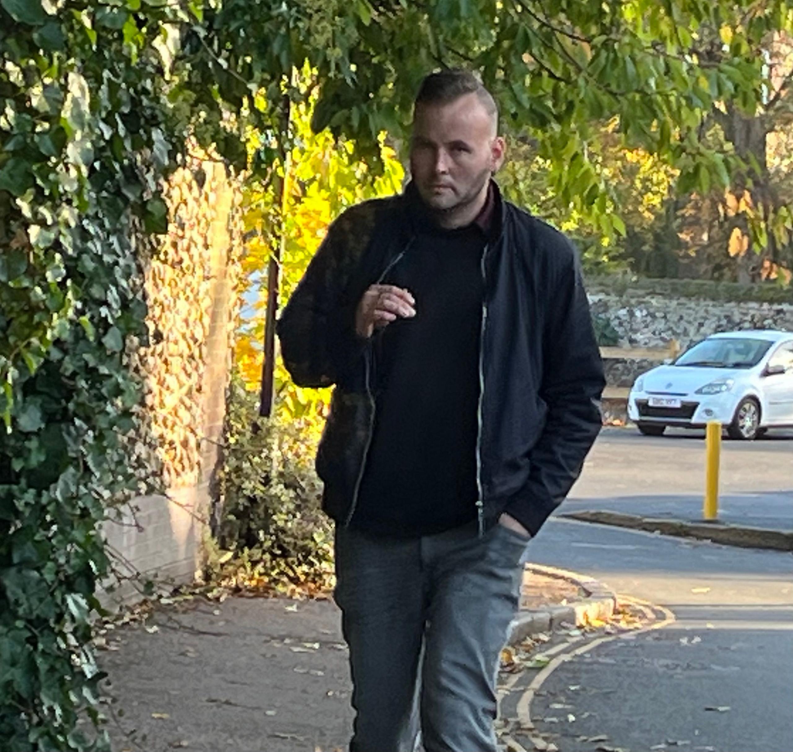 Wayne Finney arrives at Norwich Crown Court wearing all black smoking a cigarette, which he is holding in his right hand. 