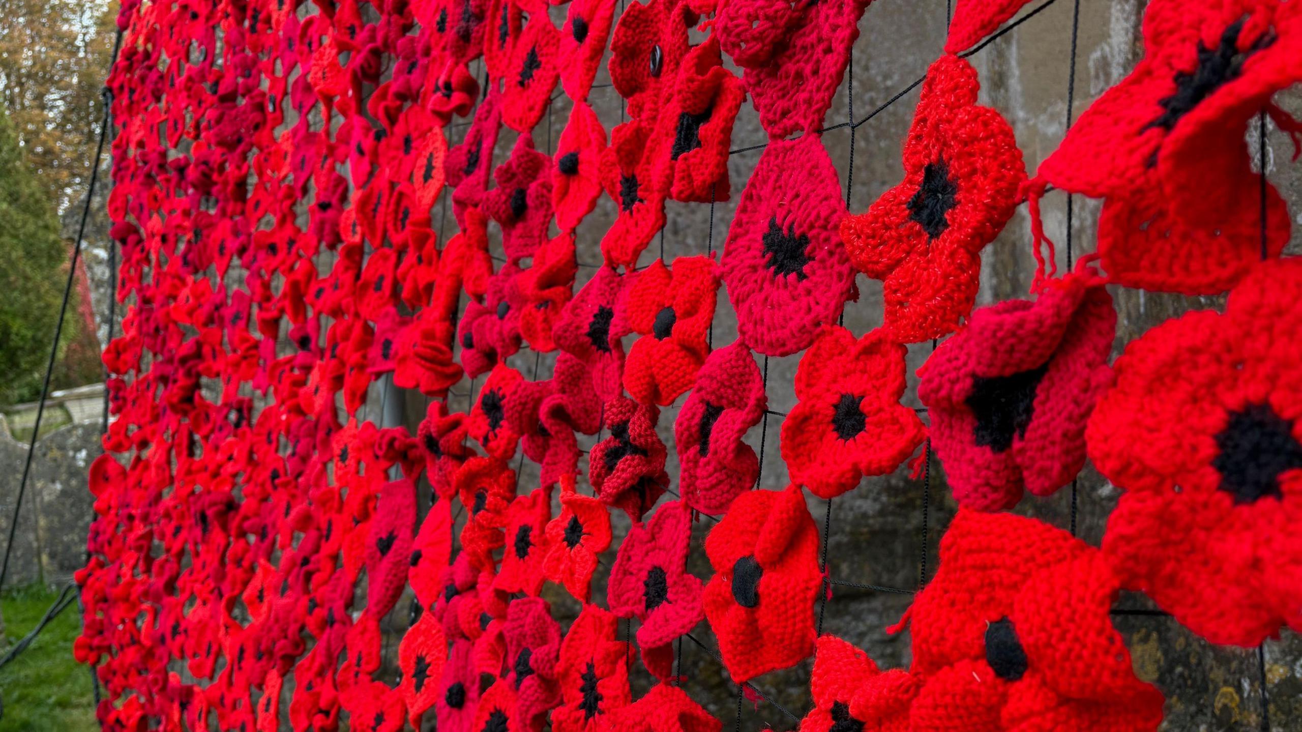 Hundreds of red knitted poppies that have been woven together attached to webbing on the side of the church building.