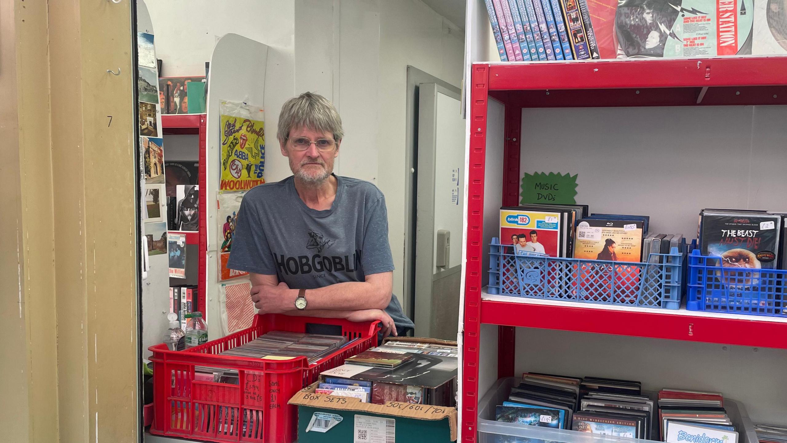 Adrian Fraser stands behind a counter in a record store. There are shelves of records to the right.