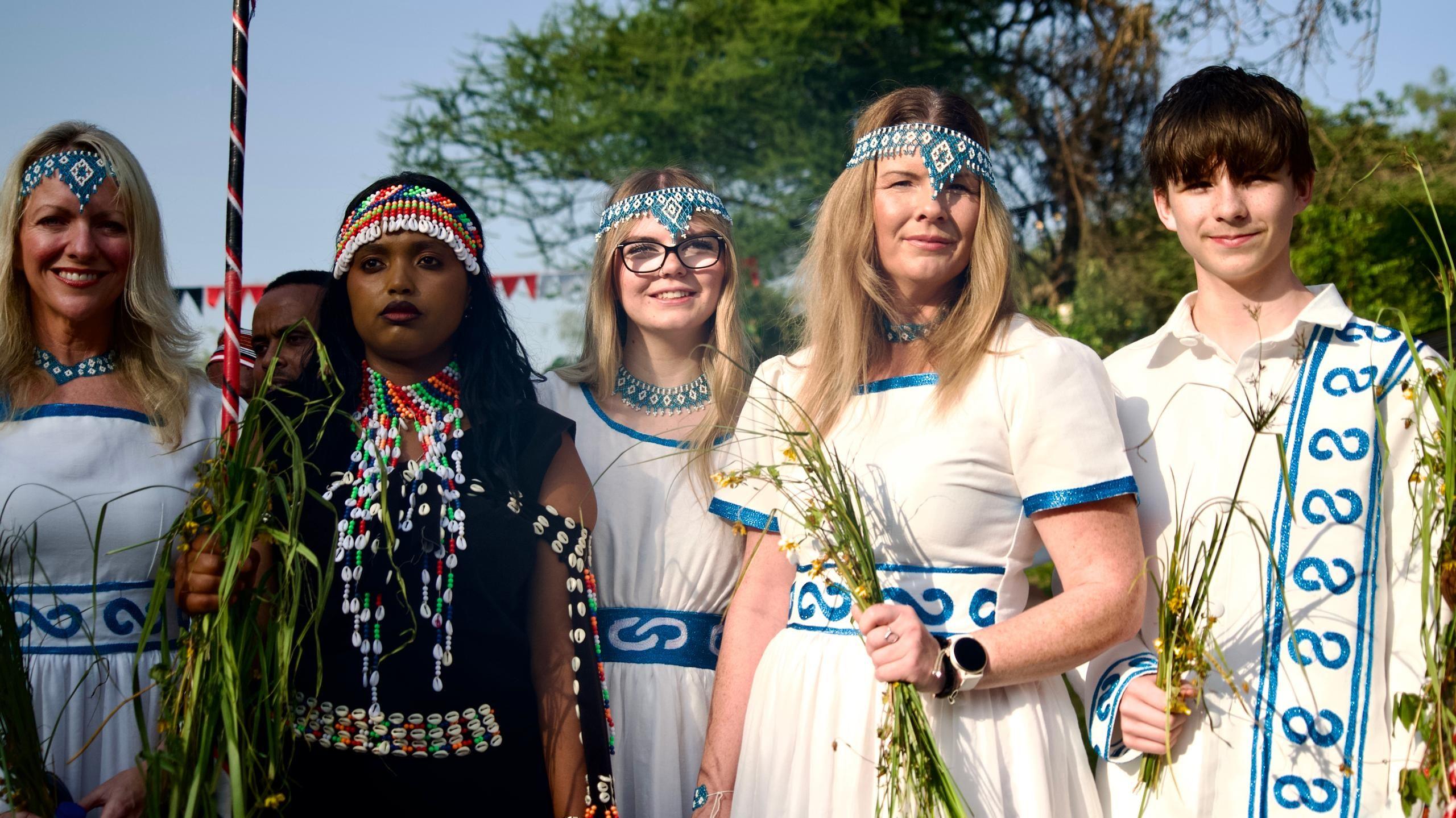 Festival attendees, adorned in jewelry, hold plants in their hands.