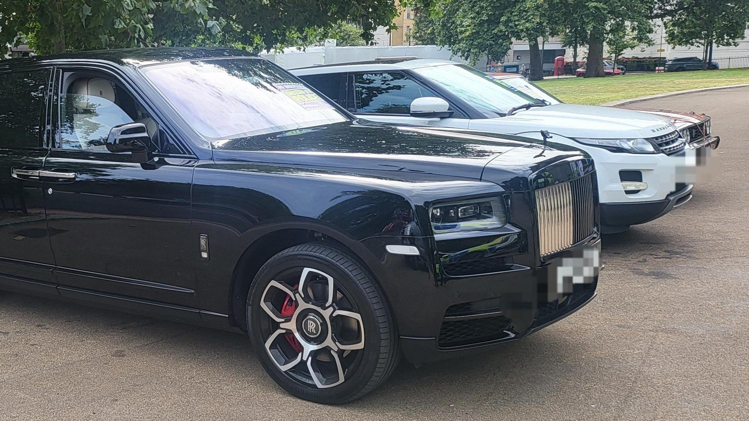 A black Rolls Royce is facing to the right of the image, next to it is a white Range Rover