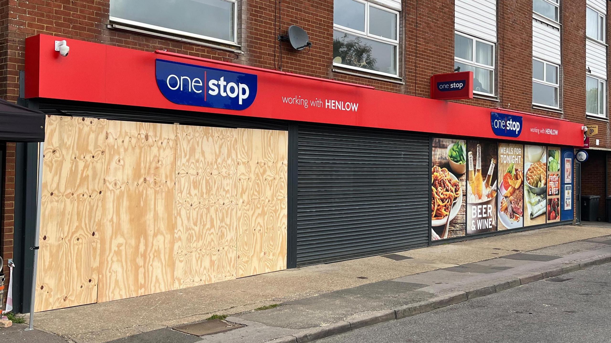 A boarded up One Stop shop which has the words "working with Henlow" written on the front.