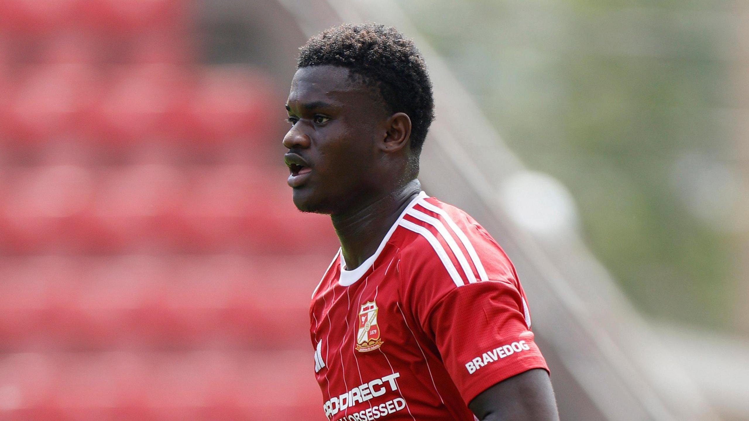 Filozofe Mabete running on the pitch wearing red Swindon Town kit during a pre-season friendly