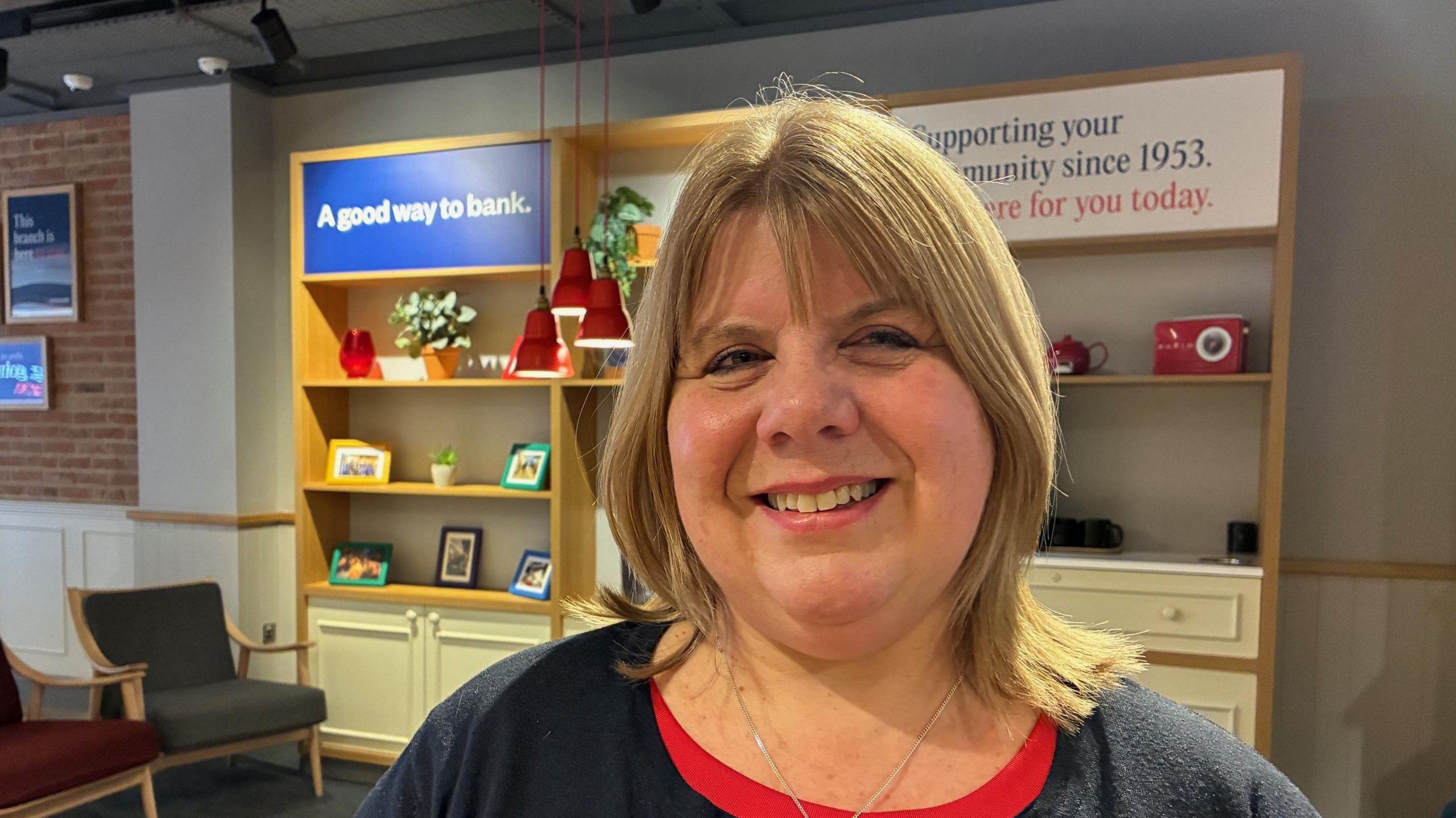 Lynn Wheeler stands in front of a display in the Nationwide branch in Reading with photos and plant pots behind her.
