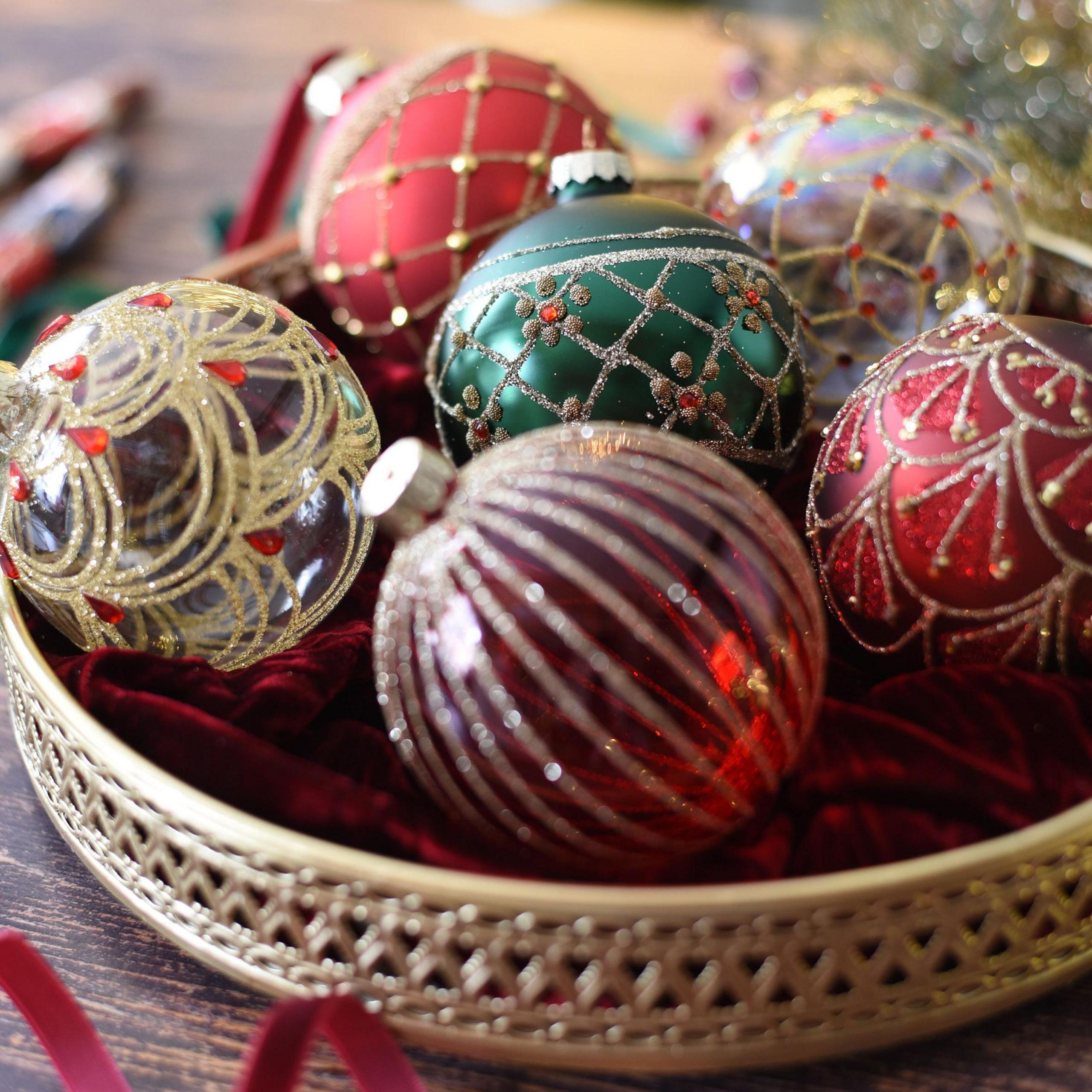 Close up of six Christmas baubles in a bowl, three of which are glass with sparkling designs on them, while two others are red with gold patterns on and the other is green