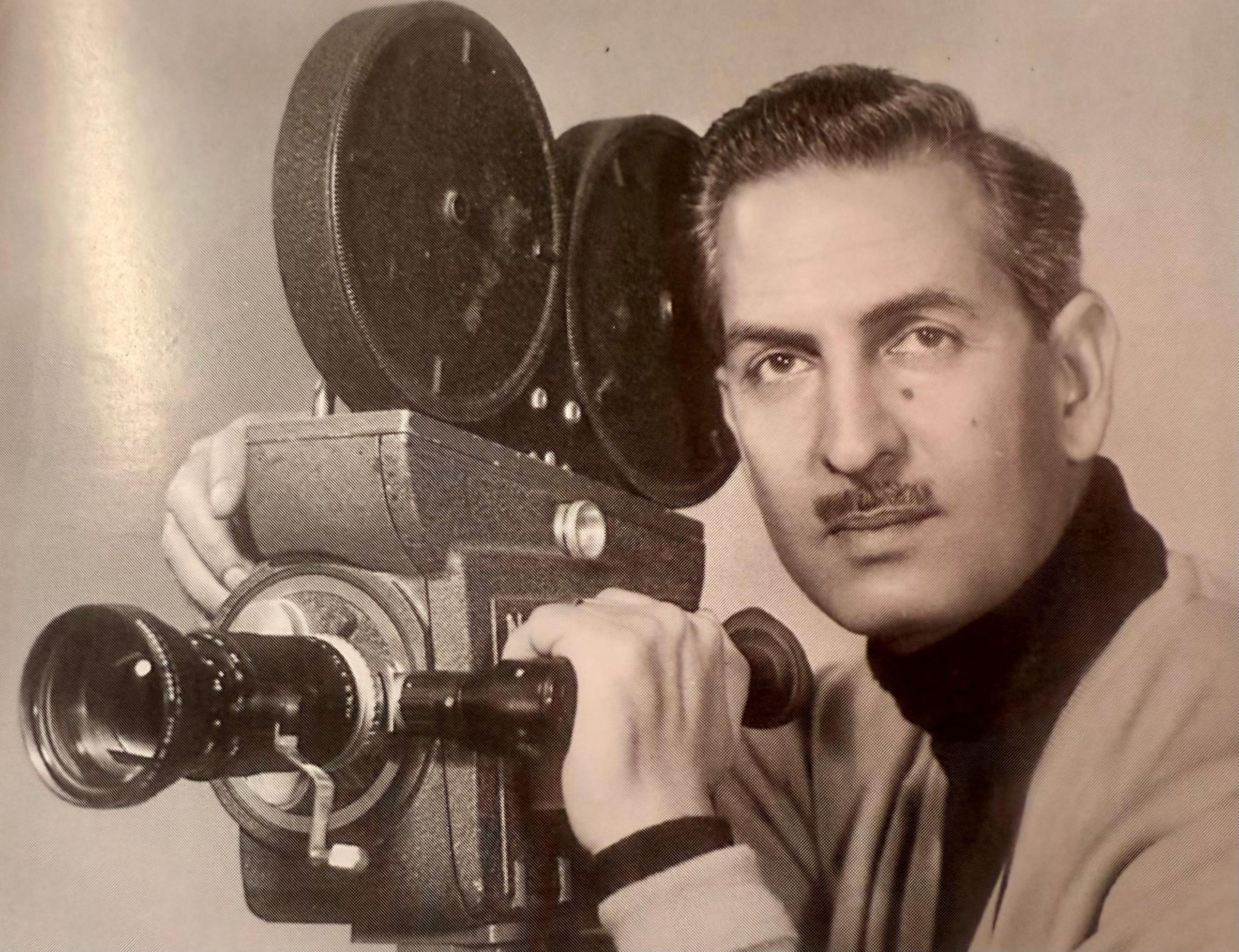 A younger Yavar pictured beside his camera from his days as cameraman and film-maker. He has a moustache and looks straight into the camera with a serious expression. 