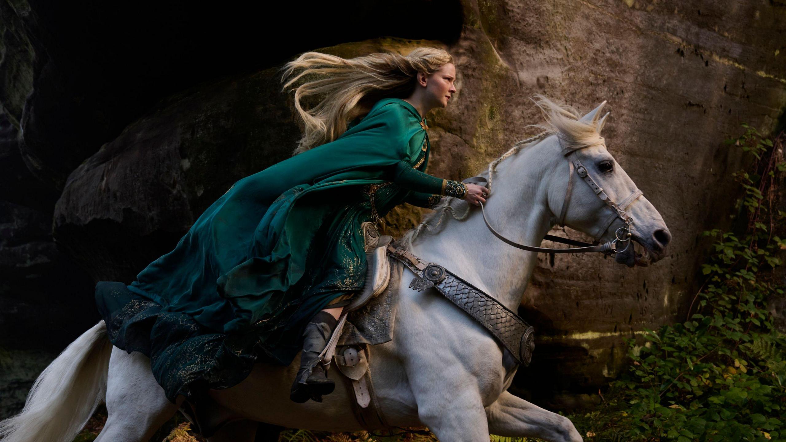 A woman wearing a green cloak, riding a white horse.