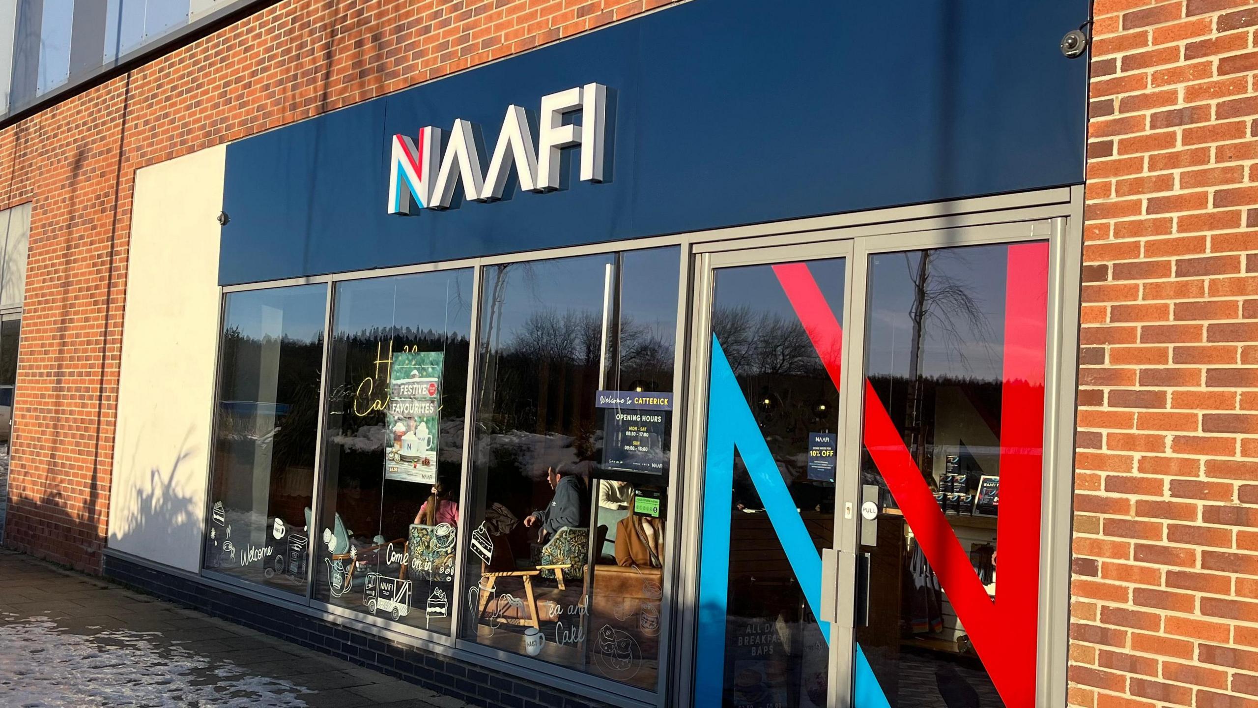 A brick building with large windows and a dark blue sign above the door which reads "NAAFI".