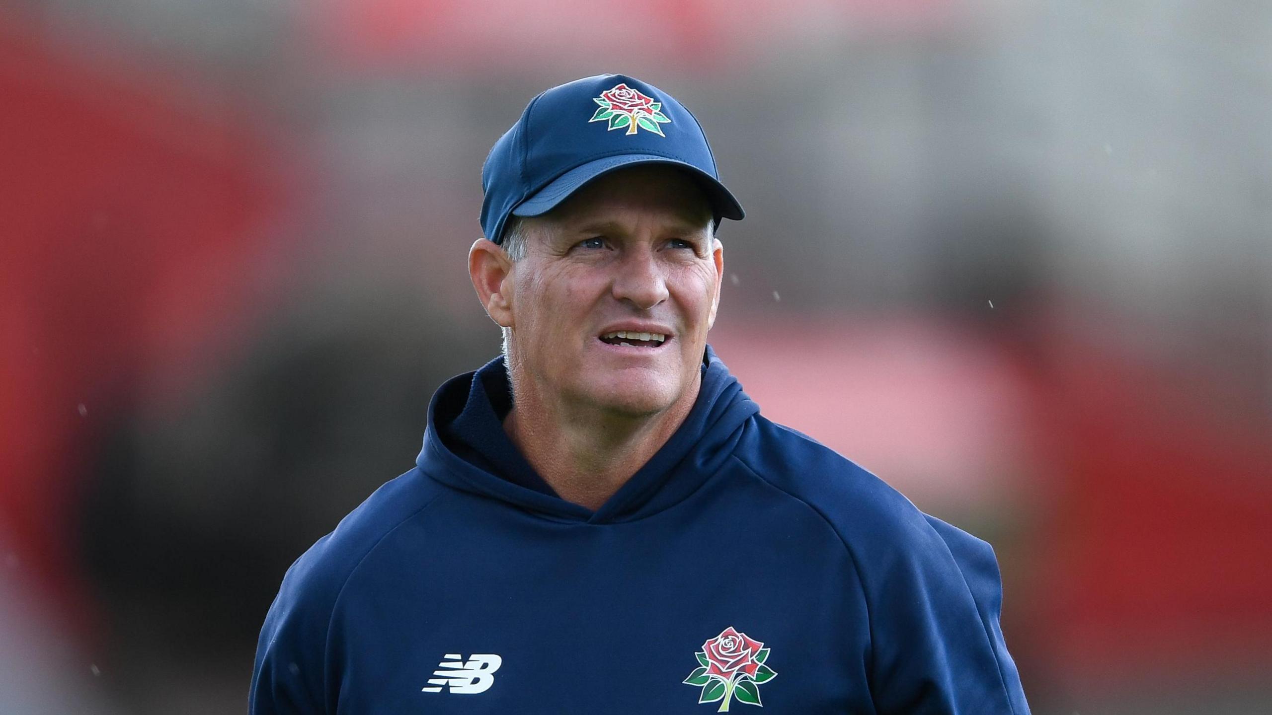 Dale Benkenstein wearing a navy blue Lancashire hoodie with a Red Rose emblem and a matching navy blue cap on a grey Manchester day 