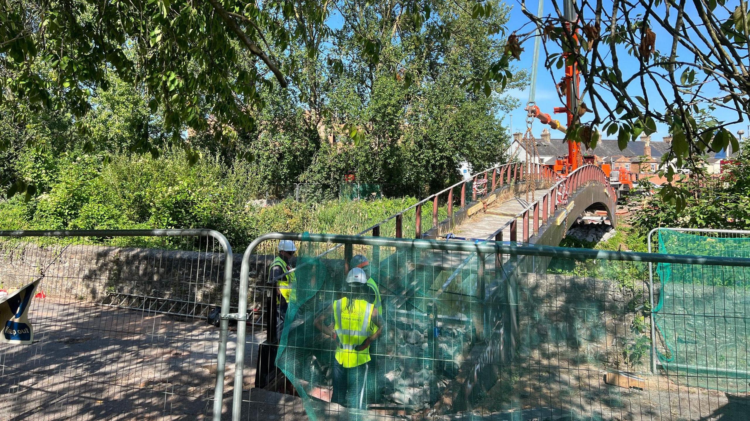 The fenced off end of the bridge, with workers and a crane ready to remove the structure.