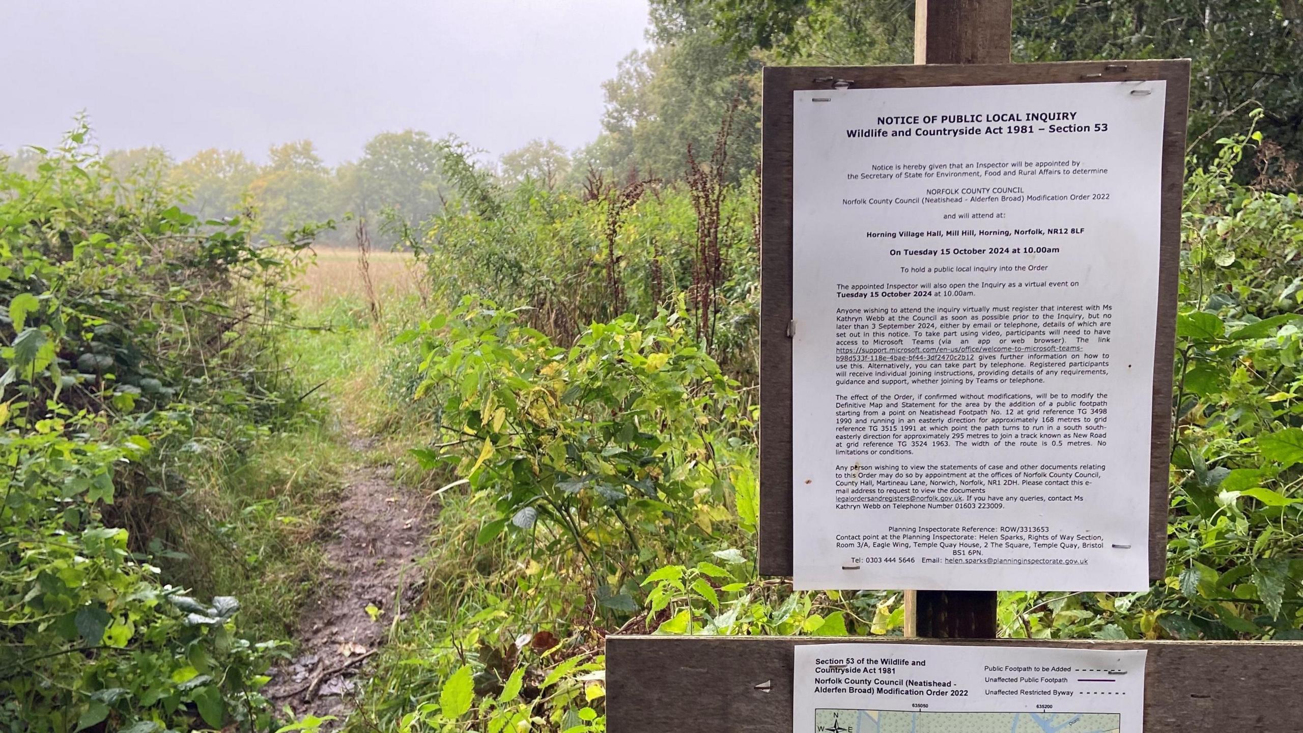 A planning inquiry notice on a post by a footpath. You can see foliage and trees in the distance.