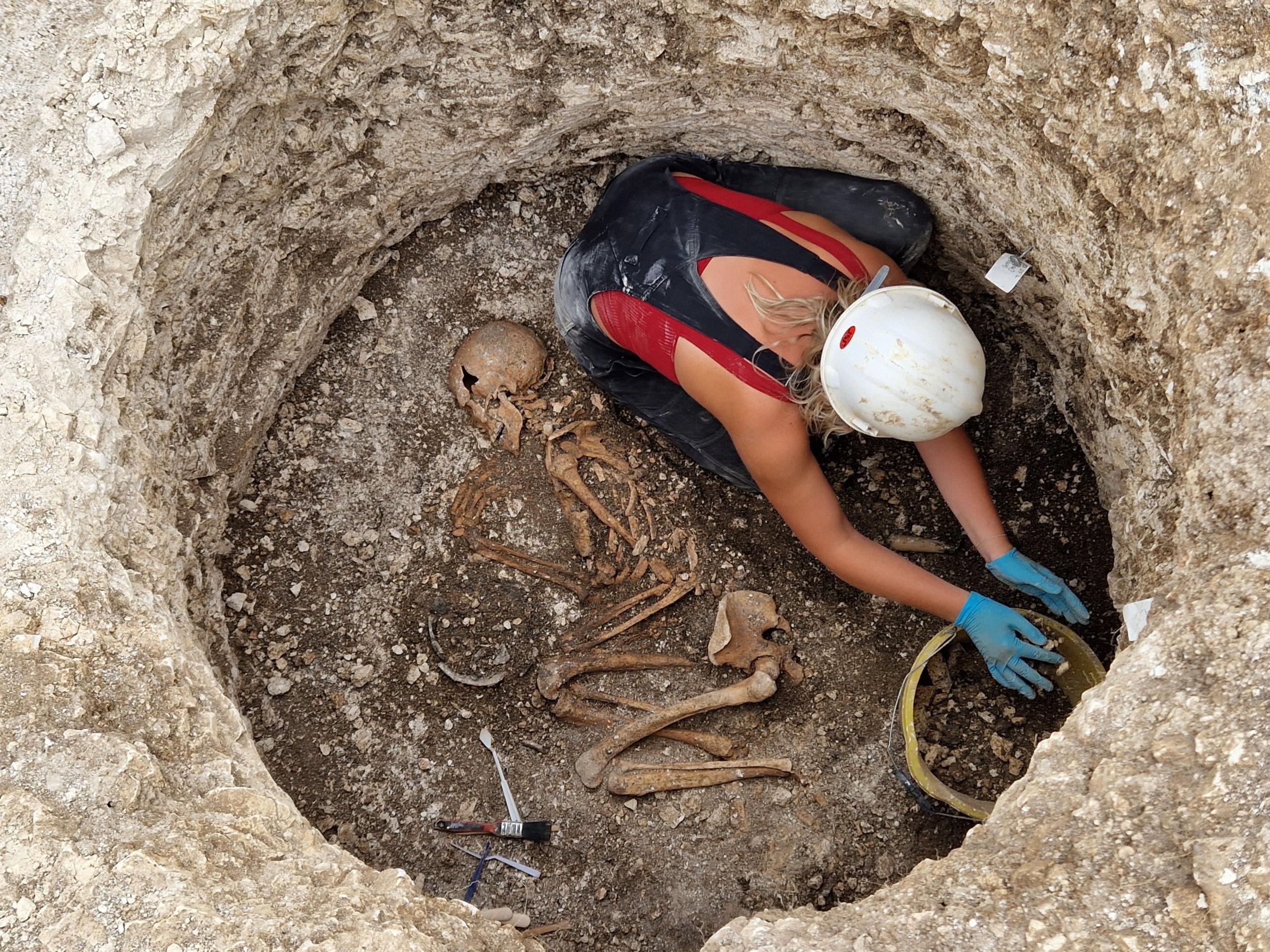 A pit in a cemetary in Dorset showing a woman digging around skeleton bones