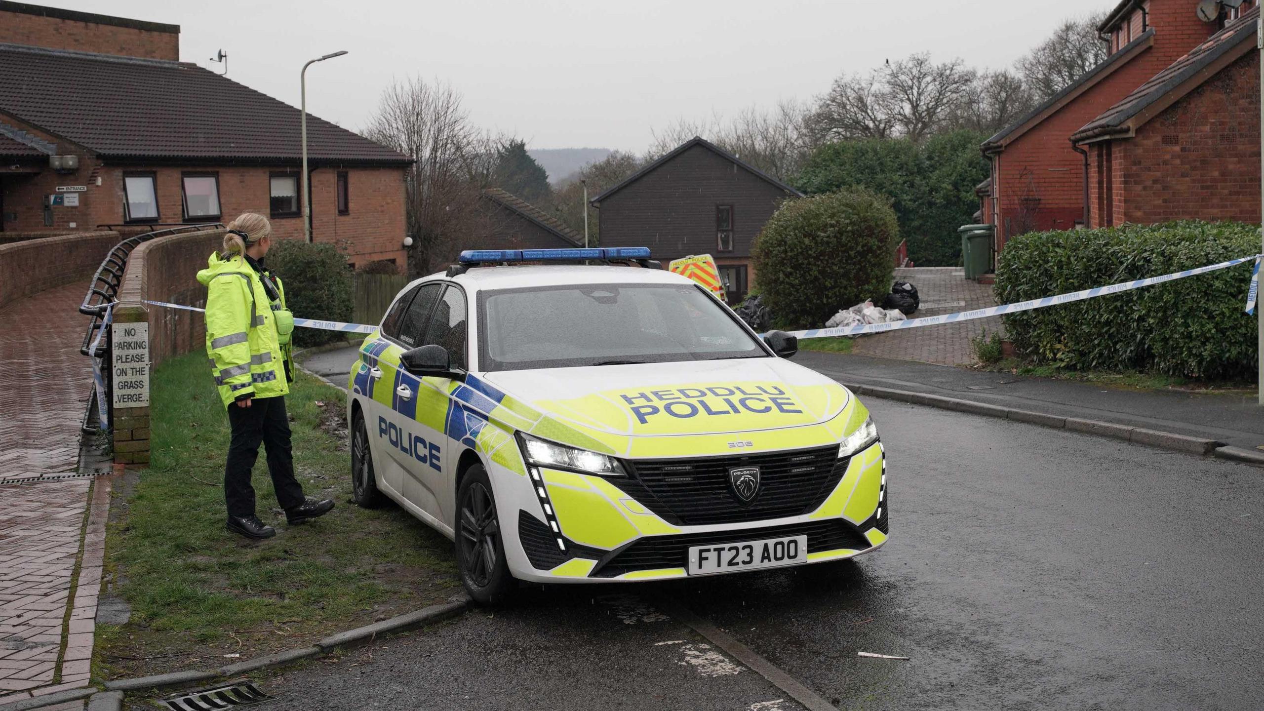 A police officer in yellow high-viz coat next to a police car