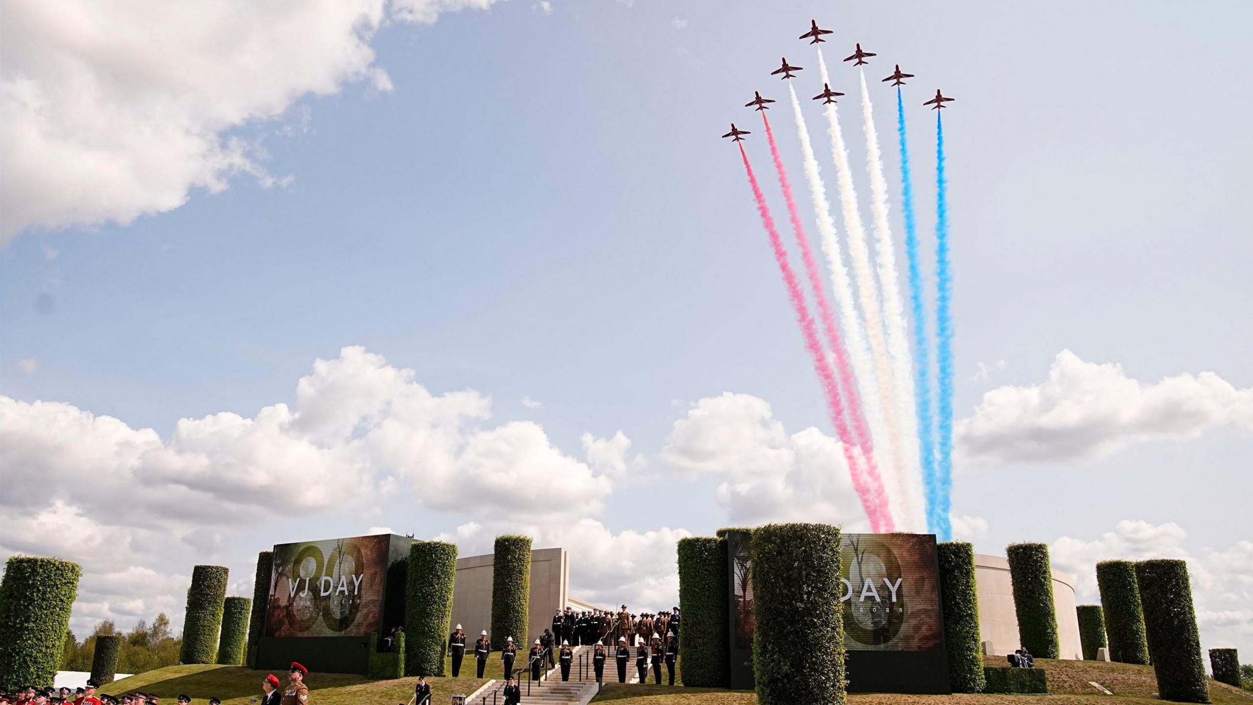 red arrows planes fly over event, with red, white and blue smoke trails