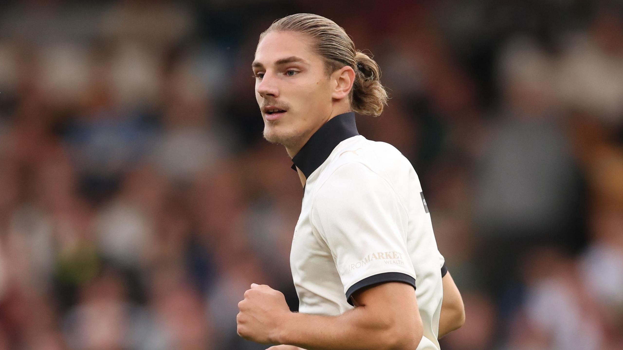 Lorent Tolaj playing for Port Vale. He has blonde hair tied back in a ponytail, and is wearing the white home kit of Port Vale.