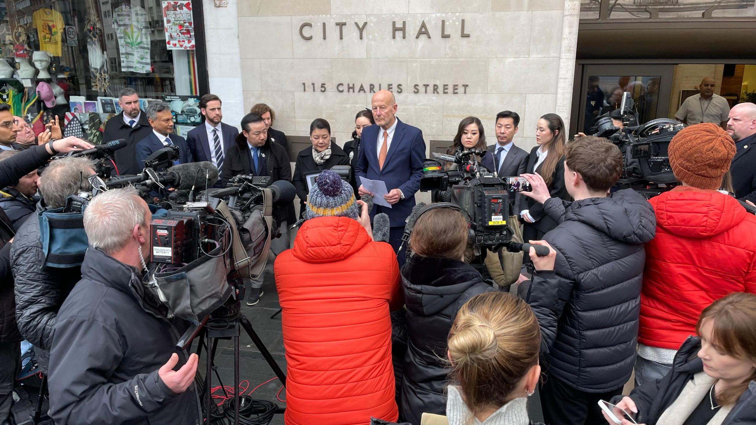 Reporters listen to a statement from family members outside Leicester City Hall