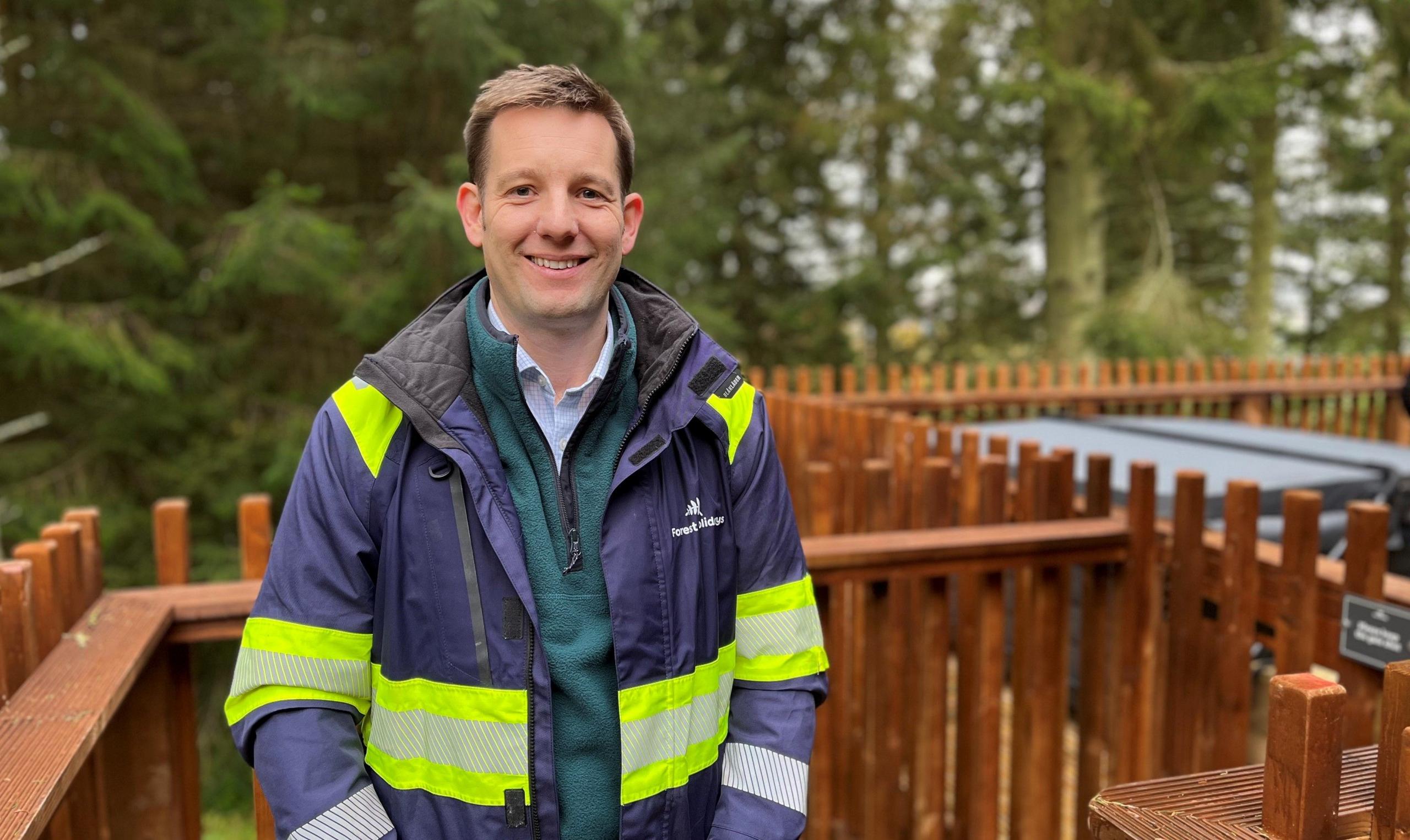 Andrew Brook, wearing a high-vis jacket, on the porch of a forest cabin with trees in the background