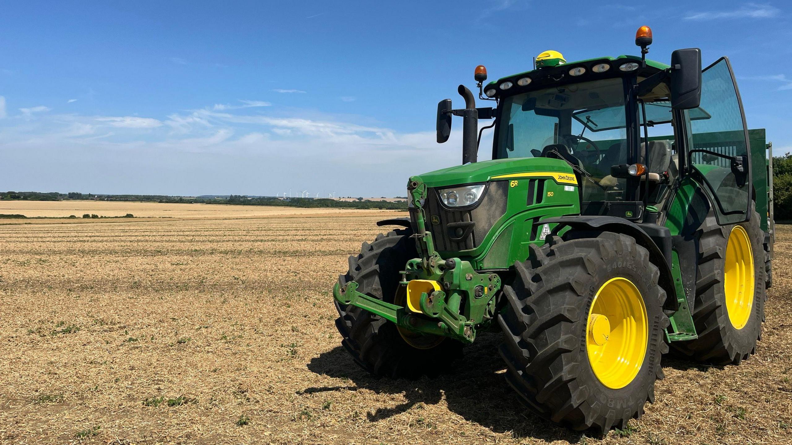 A green tractor with bright yellow wheel hubs in a field of yellow stubble