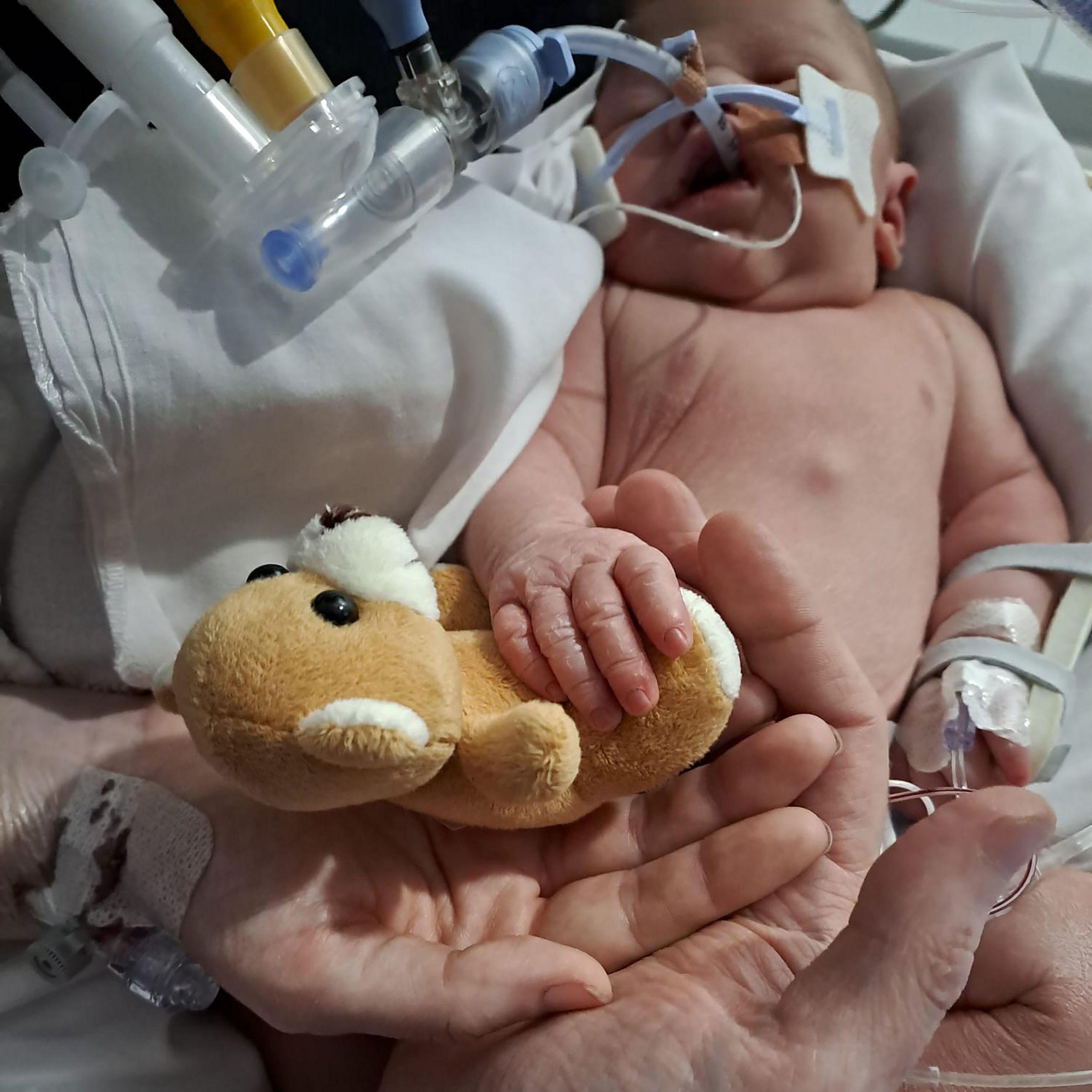 A babies hand resting on their mother and father's hands.