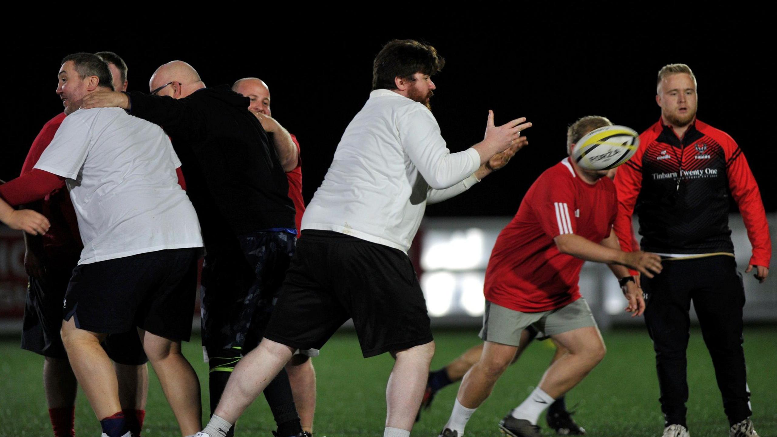 Seven members of the club mid-game. The scrum half is passing the ball from the back of a touch rugby scrum or ruck.