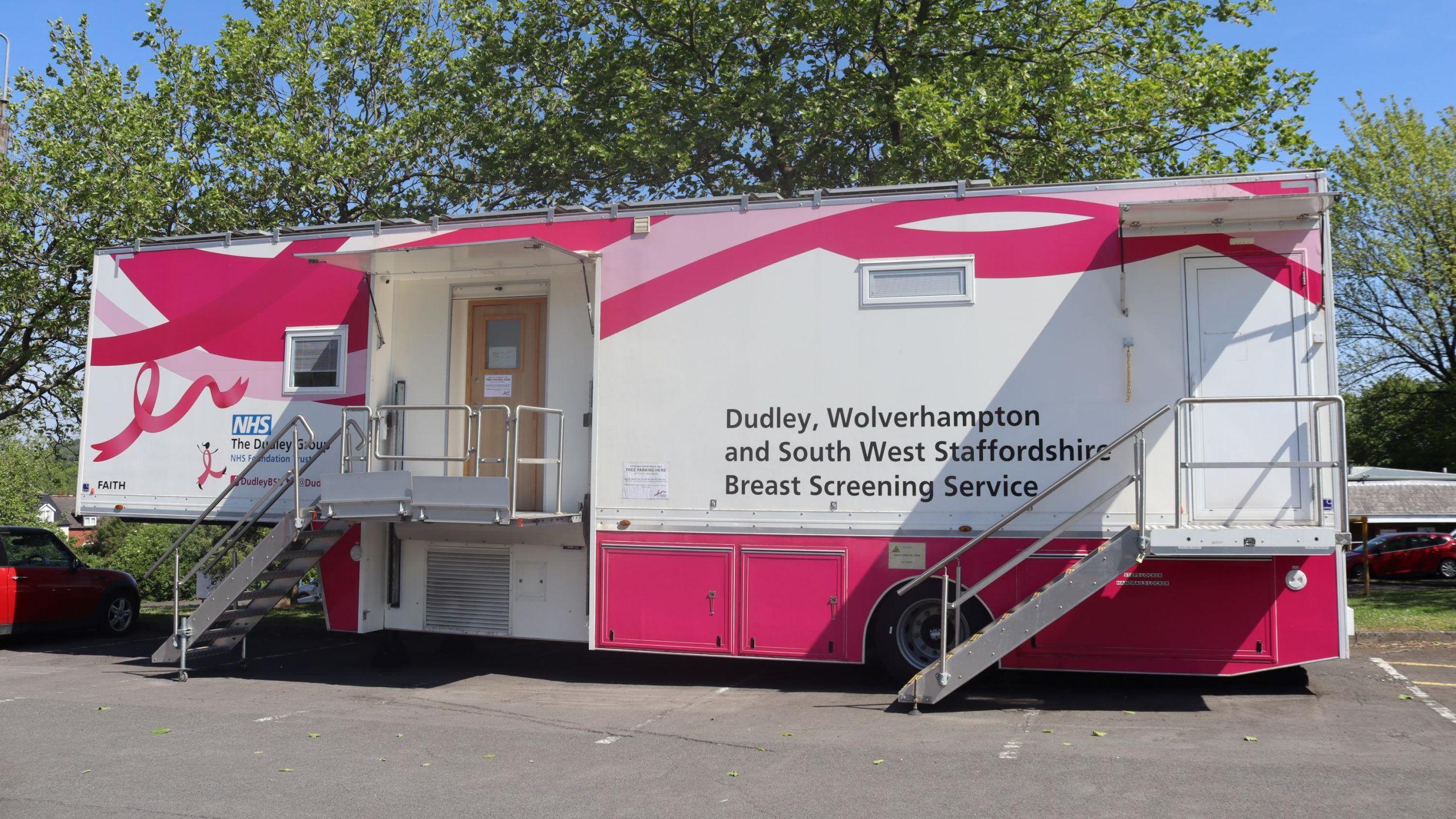 A pink and white breast cancer screening unit in a car park in front of some trees. The unit says 'Dudley, Wolverhampton and South West Staffordshire Breast Screening Service' on the front.