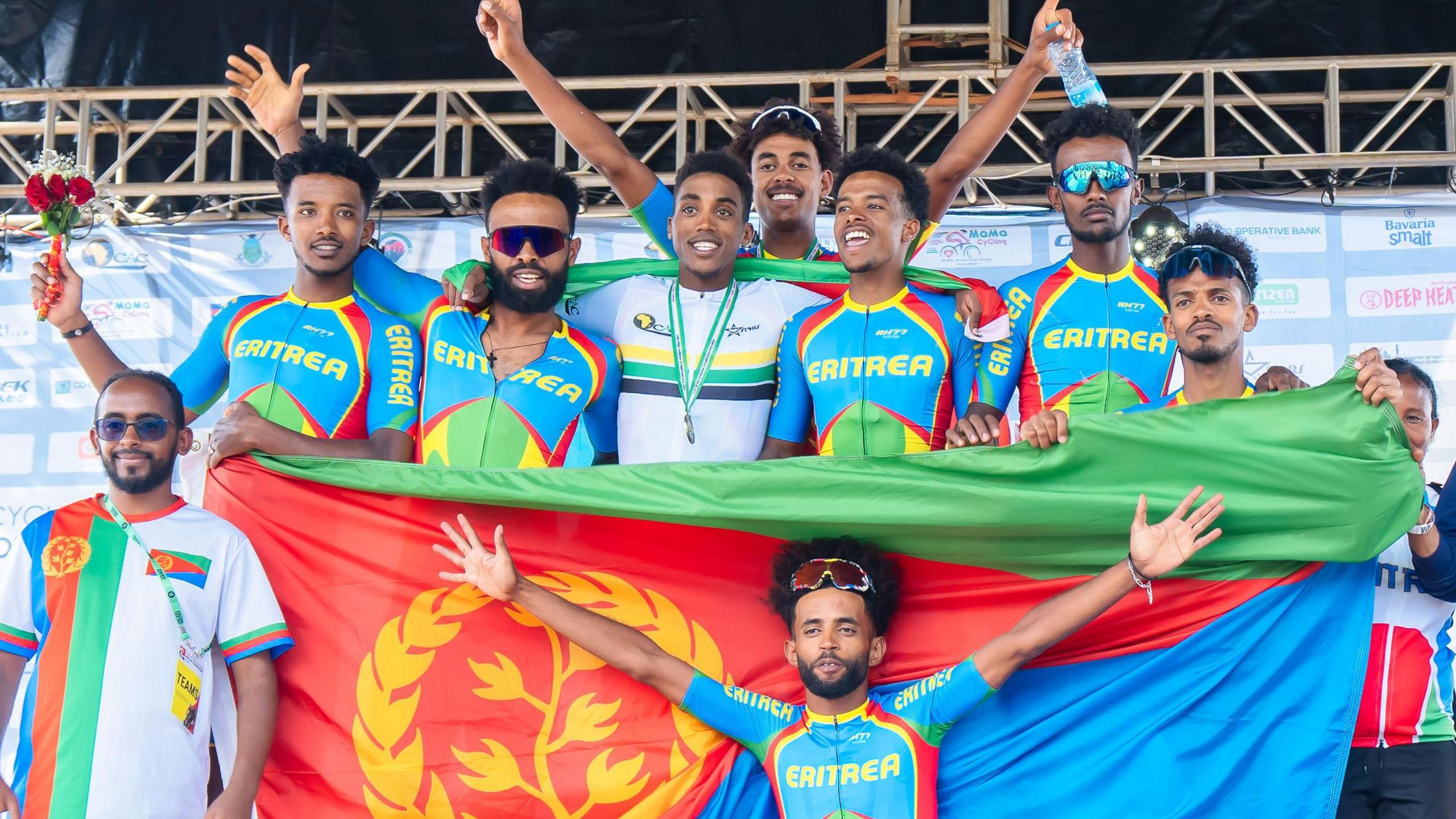 Eritrean cyclists and staff celebrate amid a giant Eritrean flag