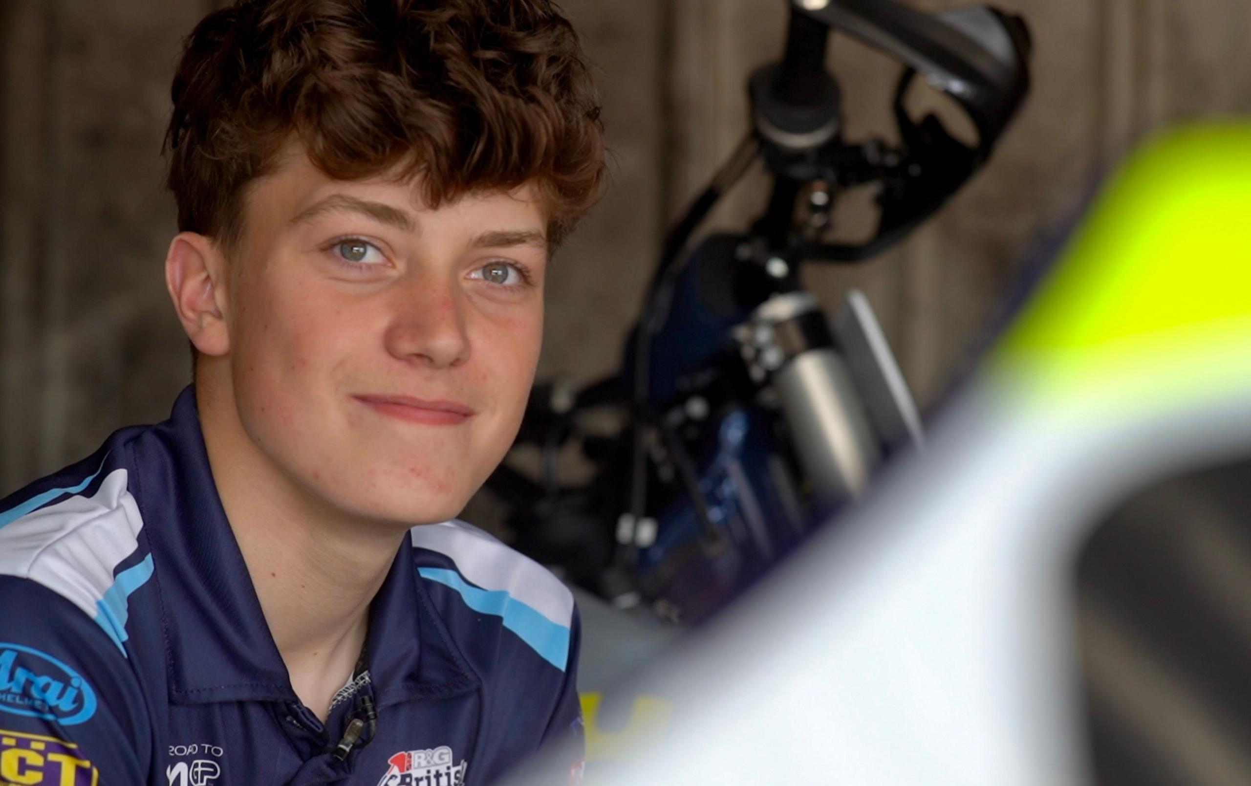 Charlie with his blue polo teamwear top, looking towards the camera. There is an out of focus part of his bike in shot.