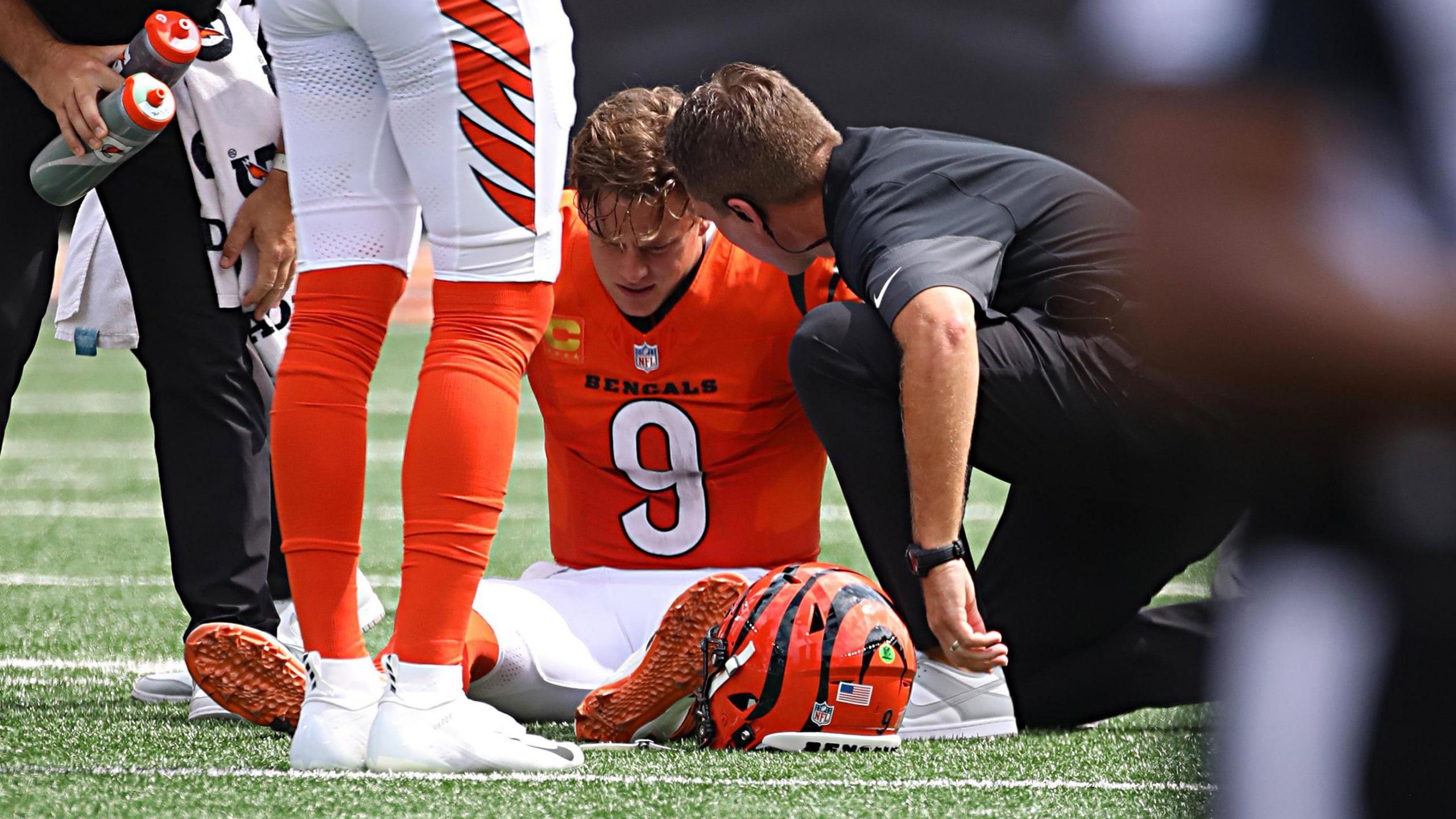 Cincinnati Bengals quarterback Joe Burrow sits on the pitch surrounded by medical staff
