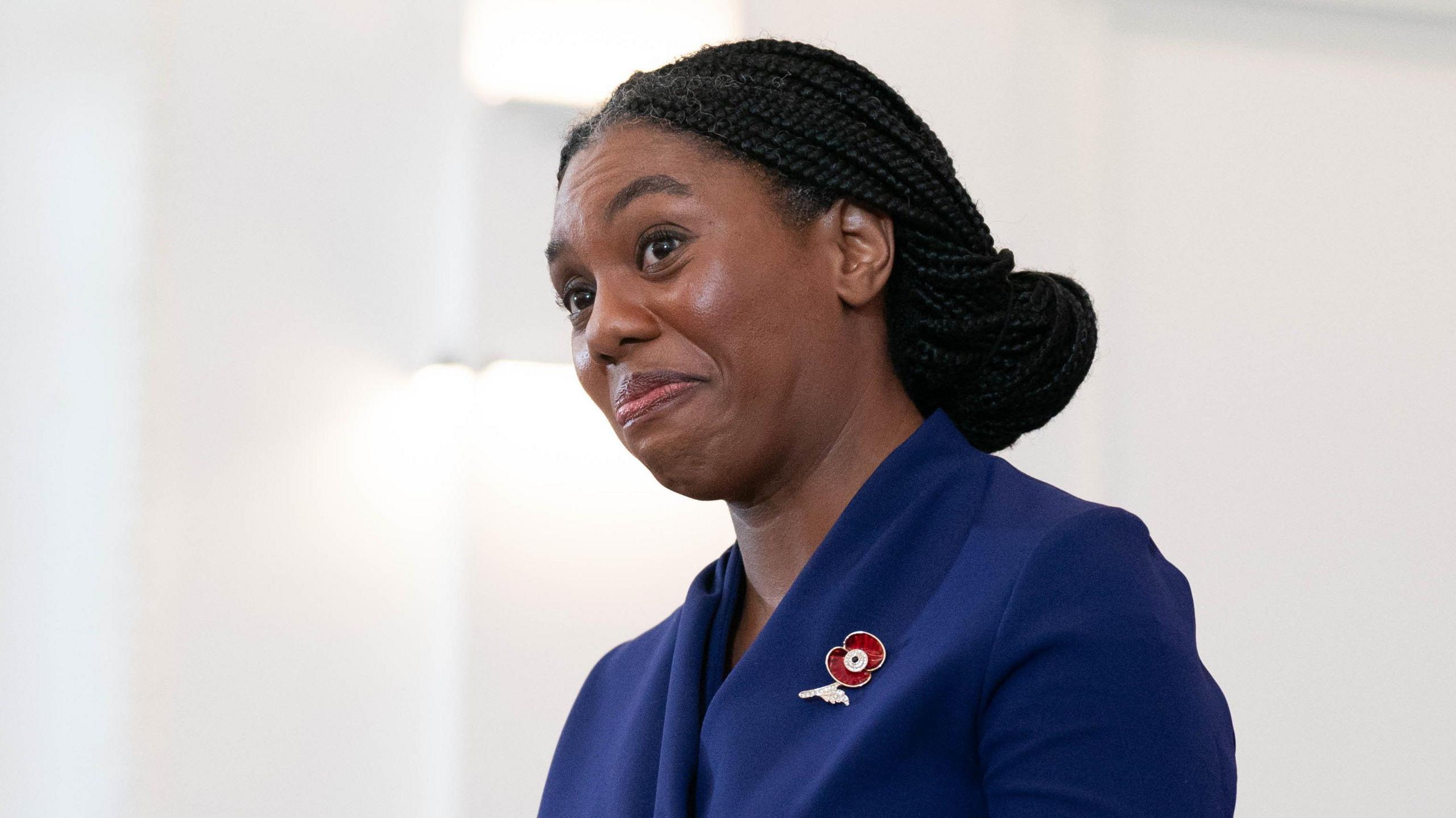 Kemi Badenoch smiles as she delivers victory speech, dressed in a blue suit with red poppy on lapel