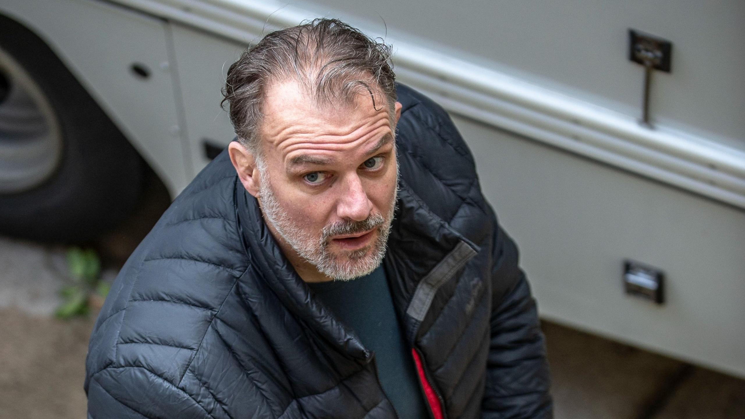 Paul Whitehurst, a white man with receding grey hair, is looking up at the camera. he is wearing a navy puffa-style jacket.