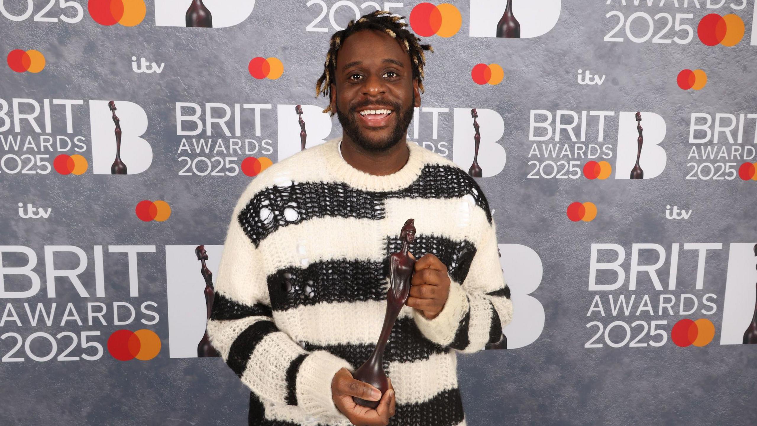 Myles Smith, in a black and white striped jumper, poses with his Brit Award in the Rising Star category