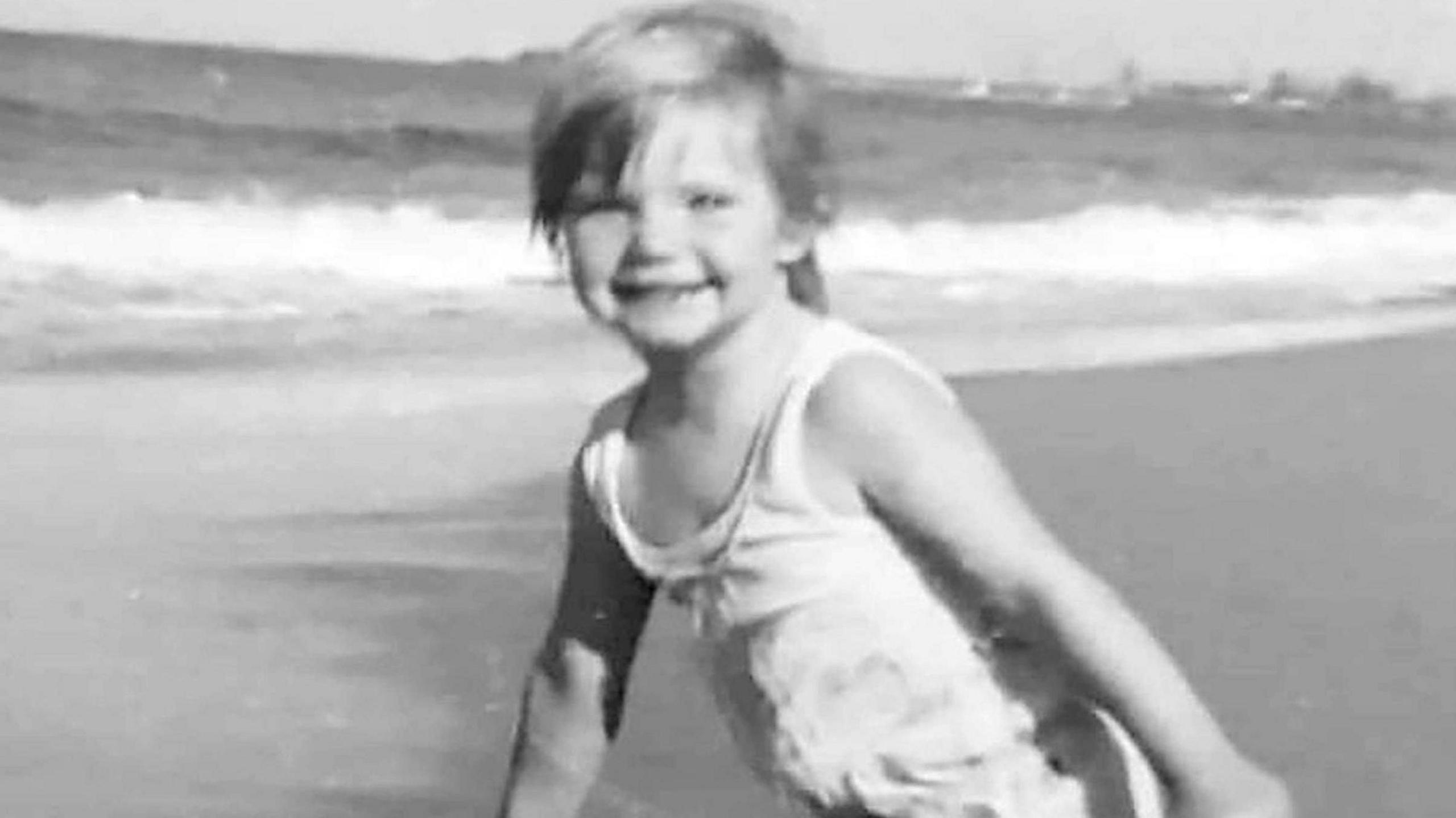 A black and white photo of a blonde girl in a swimsuit on a beach