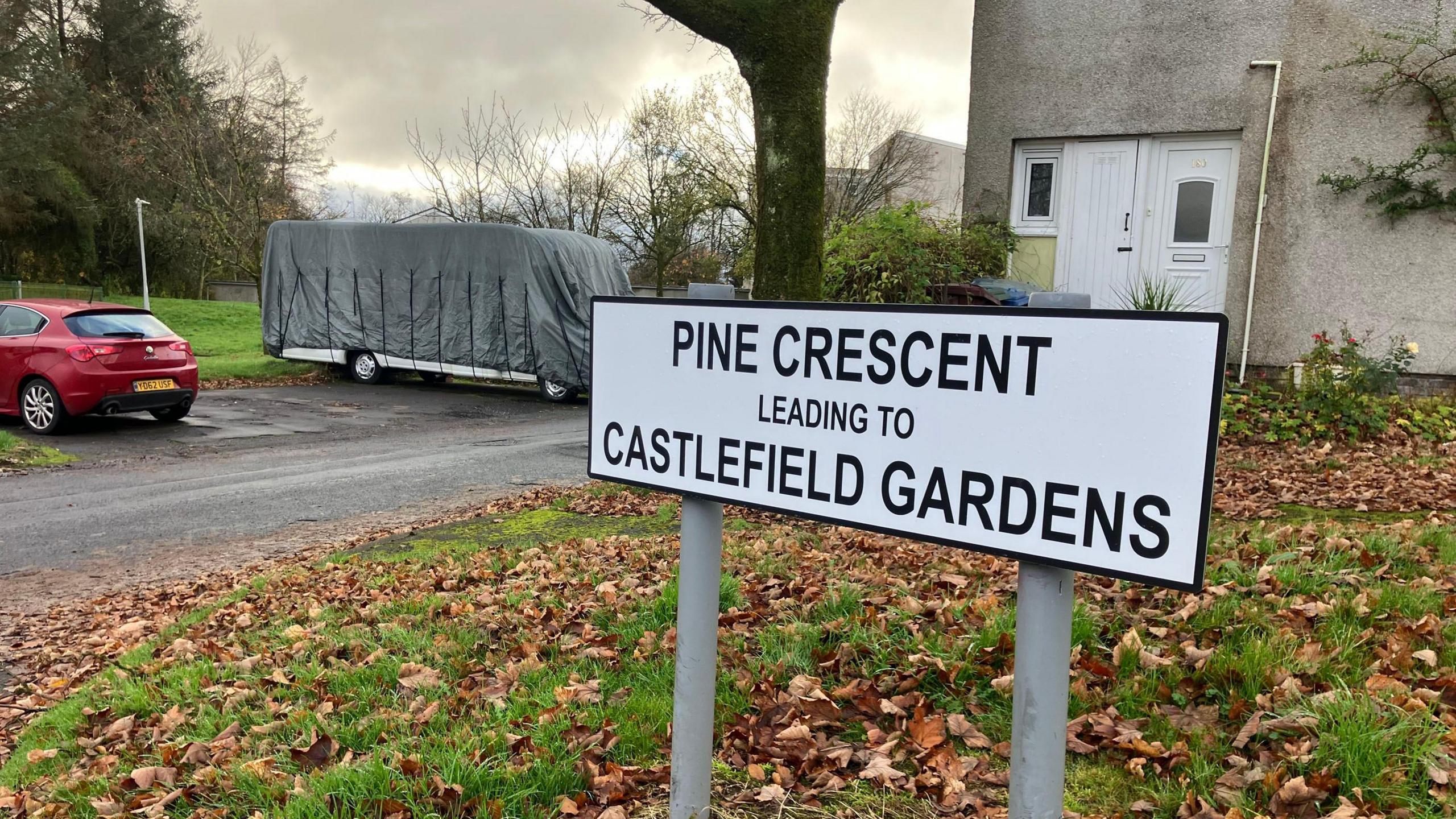 A residential area - the shot is focussed on a street sign in front of a house and tree which reads "Pine Crescent leading to Castlefield Gardens".