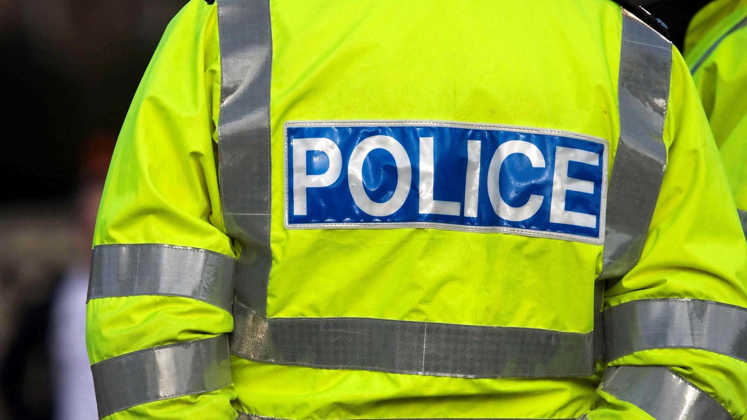 Generic image of the back of a police officer in a yellow hi-vis jacket with the words 'POLICE'
