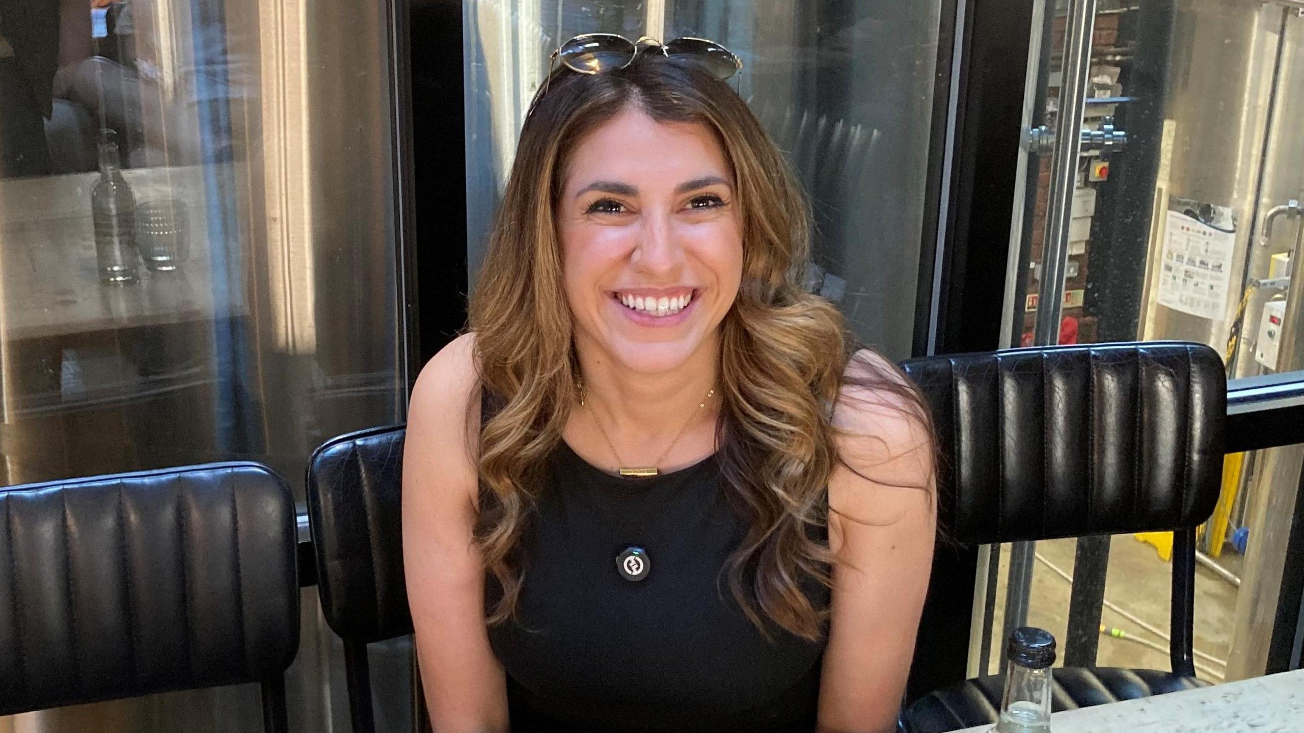Gina Earnshaw has sunglasses on her long brown hair and is wearing a black sleeveless dress