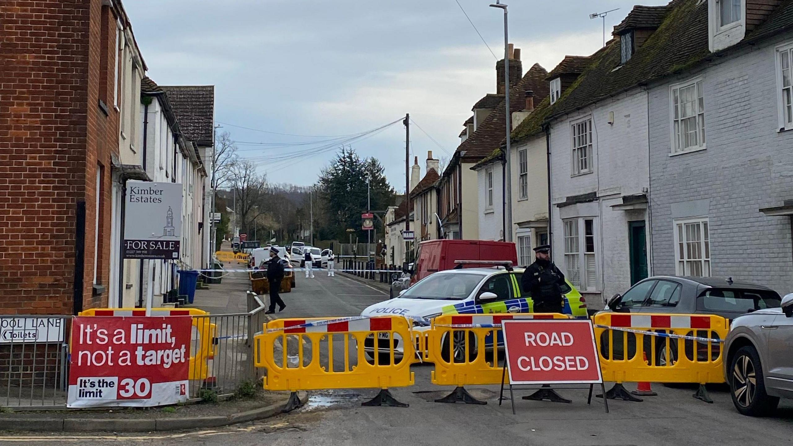 Road closure signs, barriers and police tape in place on a village street in Boughton under Blean