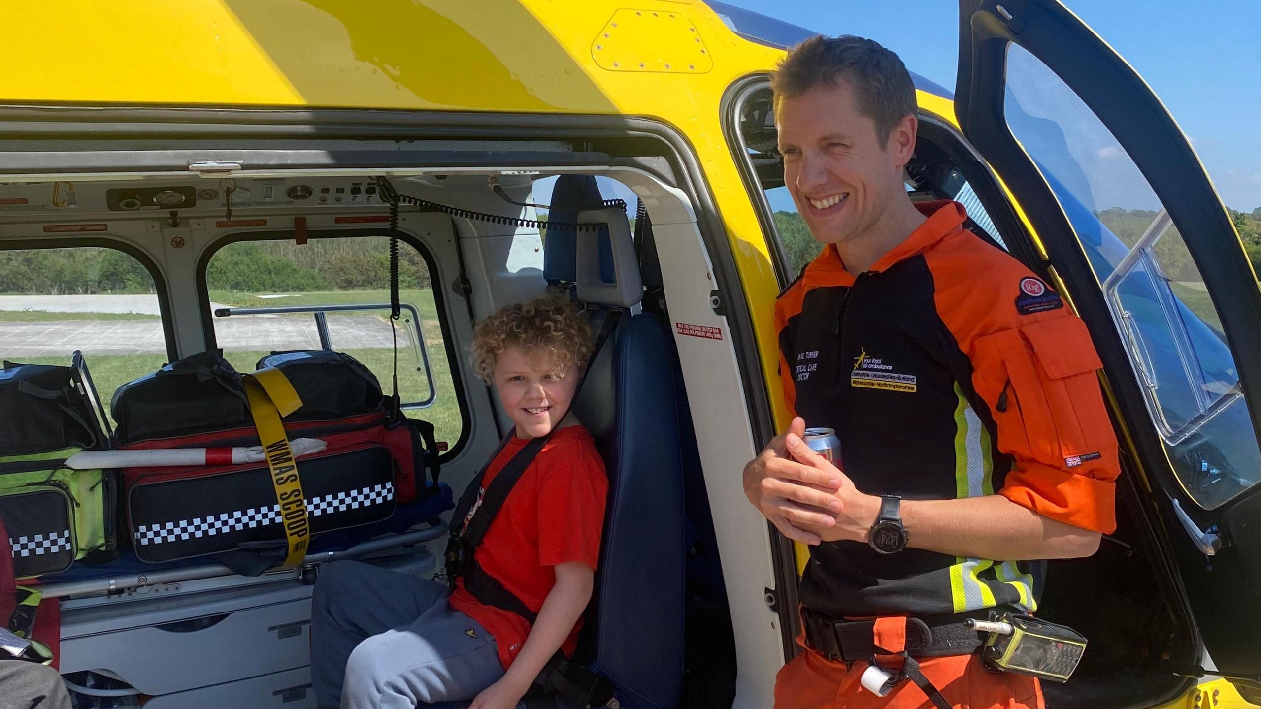 Charlie sat in a yellow air ambulance next to a crew member who is holding a can