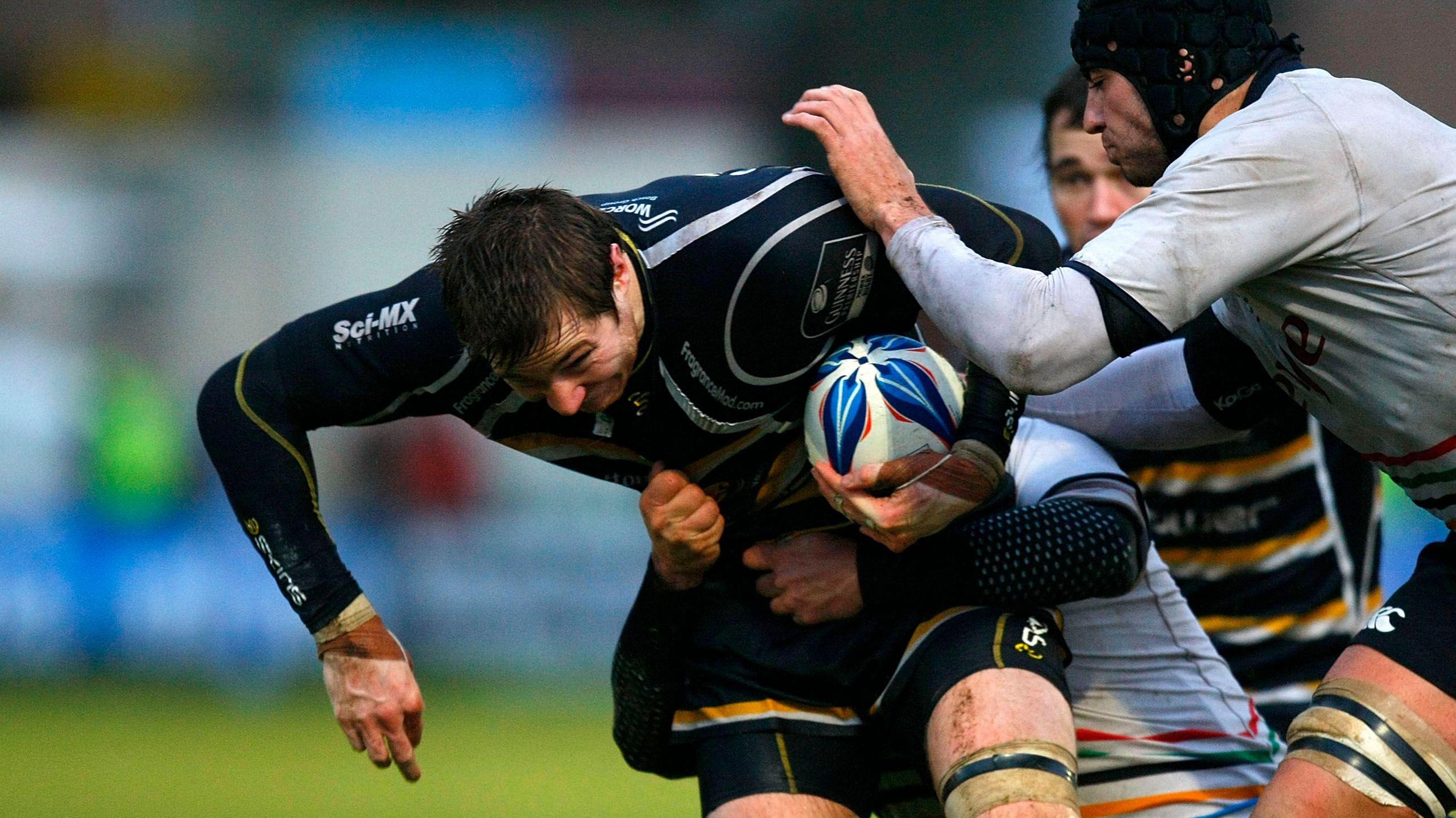 James Collins, clutching the ball under his left arm, is tackled by opponents during a match