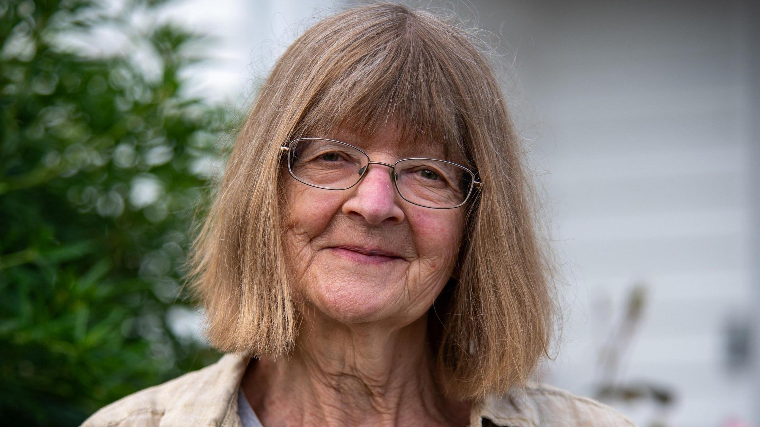 A head and shoulder photograph of an older white lady wearing glasses and fair brown hair cut in a bob style with a fringe