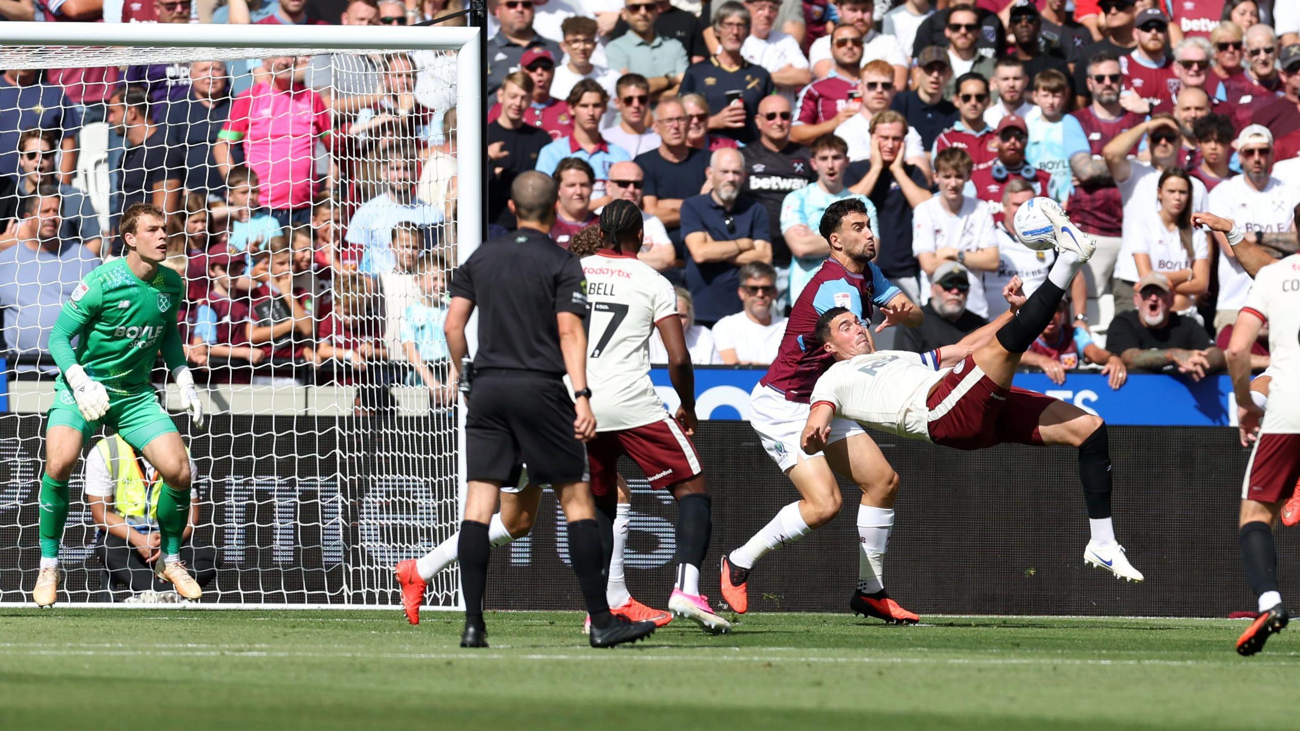 Footballer Lloyd Jones scores with an overhead kick while playing for Charlton Athletic Football Club at West Ham in the EFL Championship at the London Stadium and wearing a white shirt with dark red shorts against opponents in claret and blue shirts and white shorts with a crowd watching on