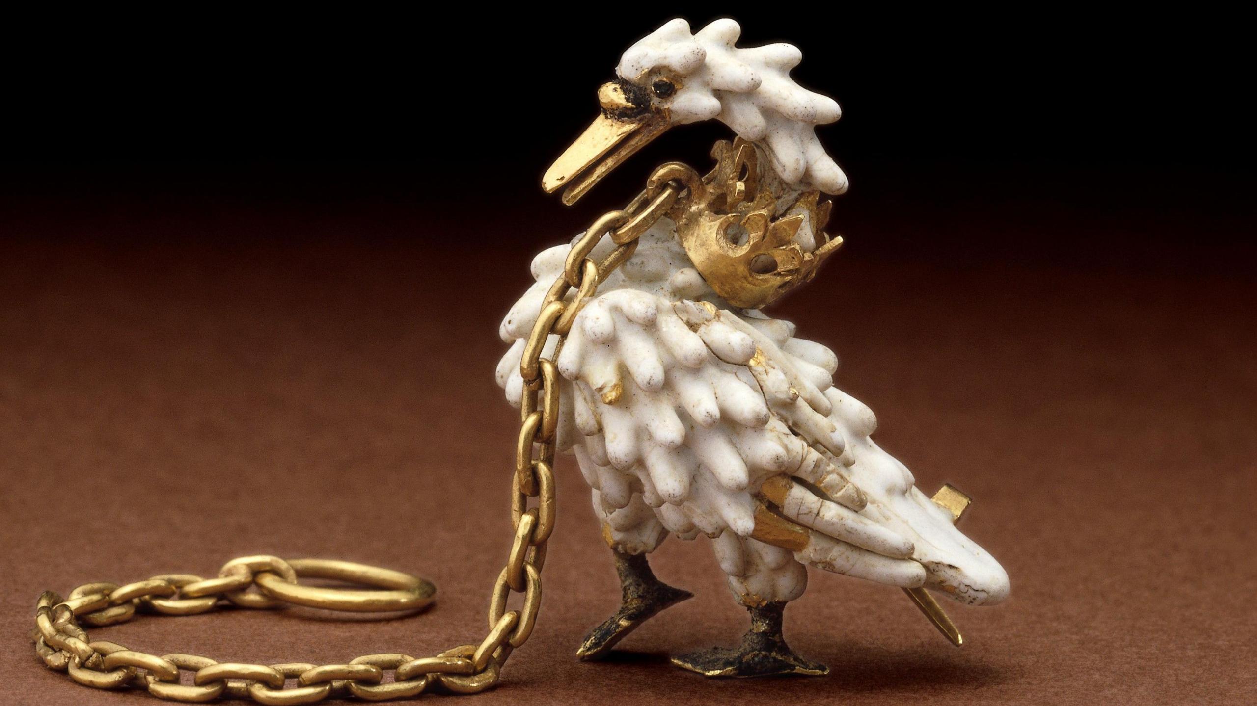 A brooch of a swan with a gold coronet around its neck and a gold chain. The beak and feet of the swan are gold while the body is made of enamel.